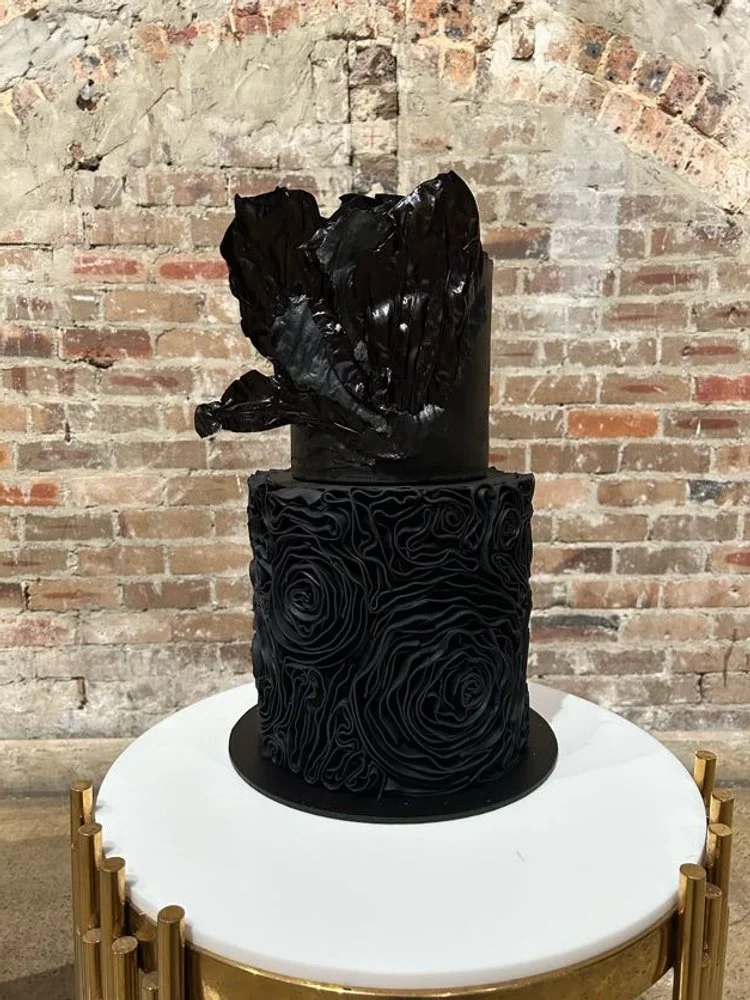 Black wedding cakes on a white table with a brick wall background.