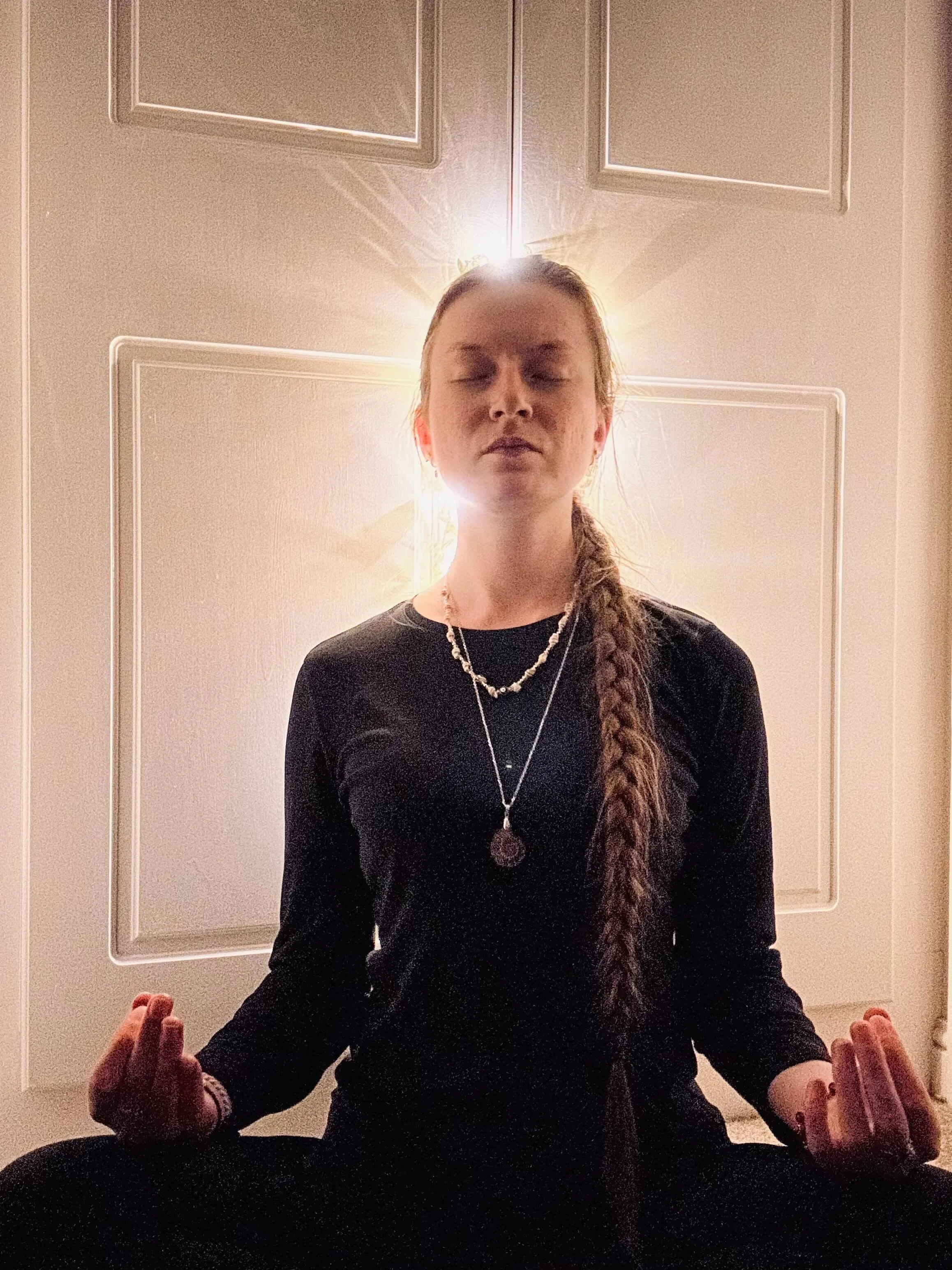 Woman meditating in lotus pose with closed eyes, light glowing behind her head, representing calm and mindfulness during sound therapy.