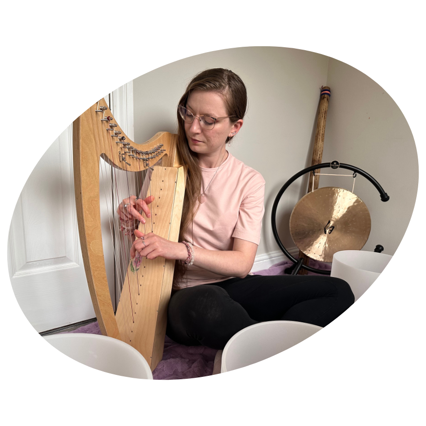 Sound therapist playing a wooden harp surrounded by crystal singing bowls and a gong during a therapeutic music session.