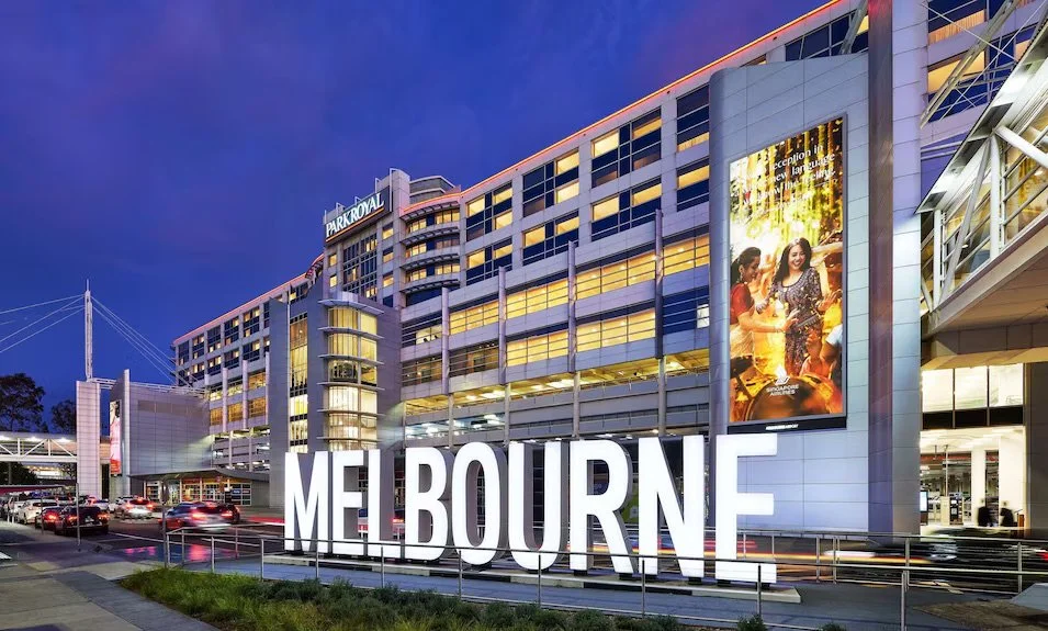 Night view of the Melbourne Park Royal hotel with illuminated signs, modern architecture, and a digital billboard displaying a movie scene.