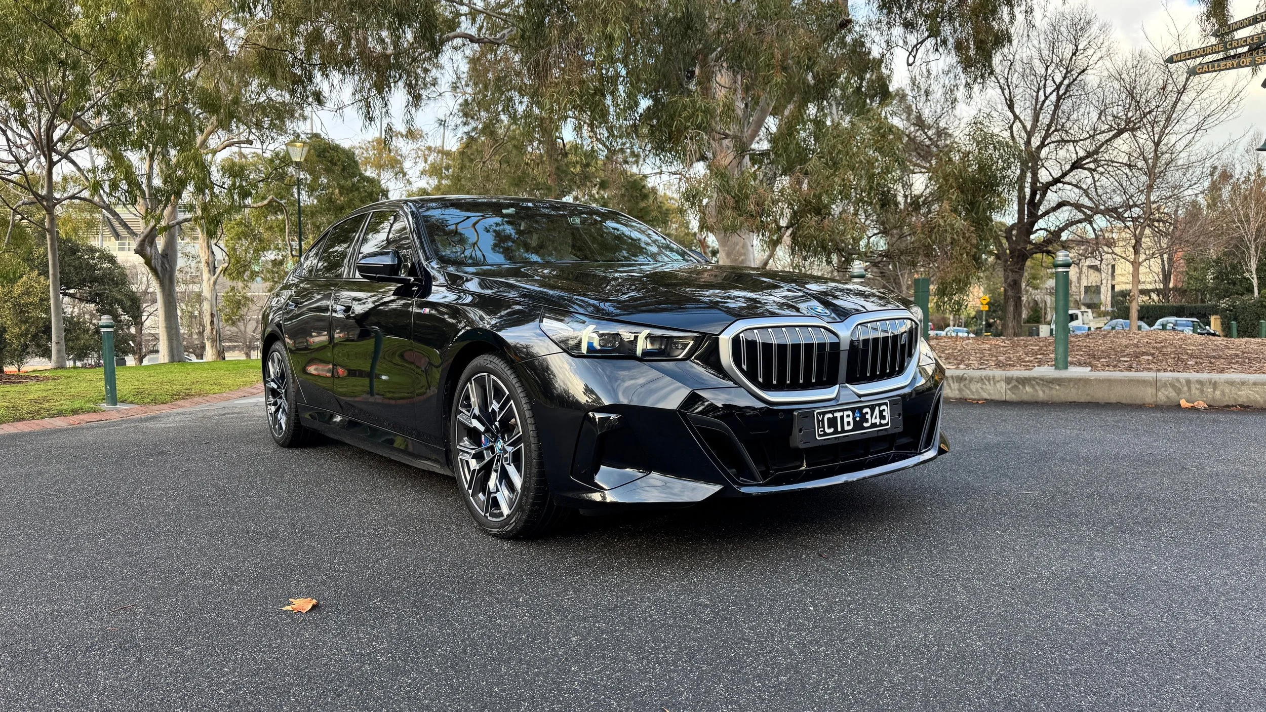 GM Drive. A black BMW sedan parked on a street with trees and park area in the background.