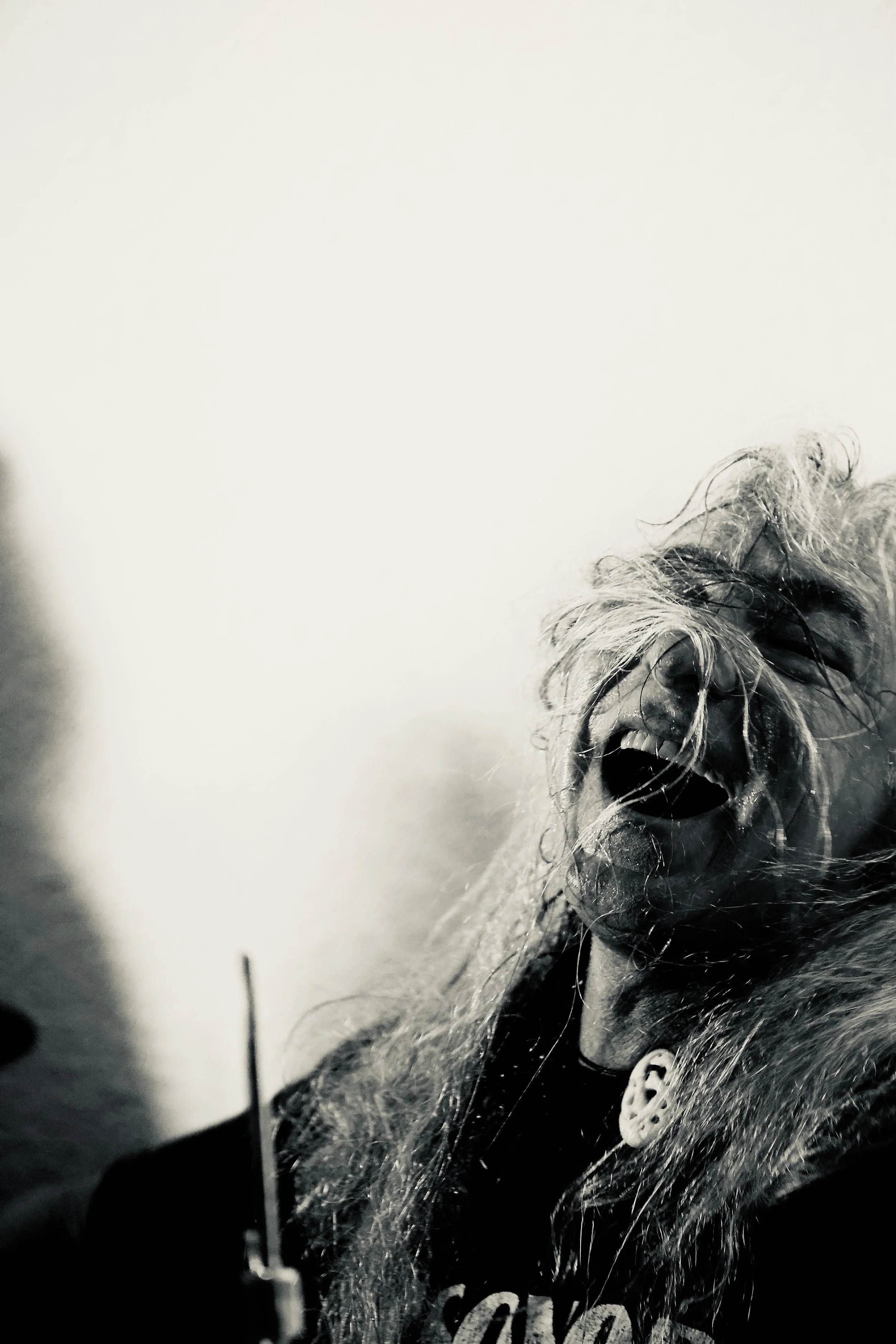 Une personne avec des cheveux longs et désordonnés, criant ou hurlant avec une expression intense sur le visage, en noir et blanc.