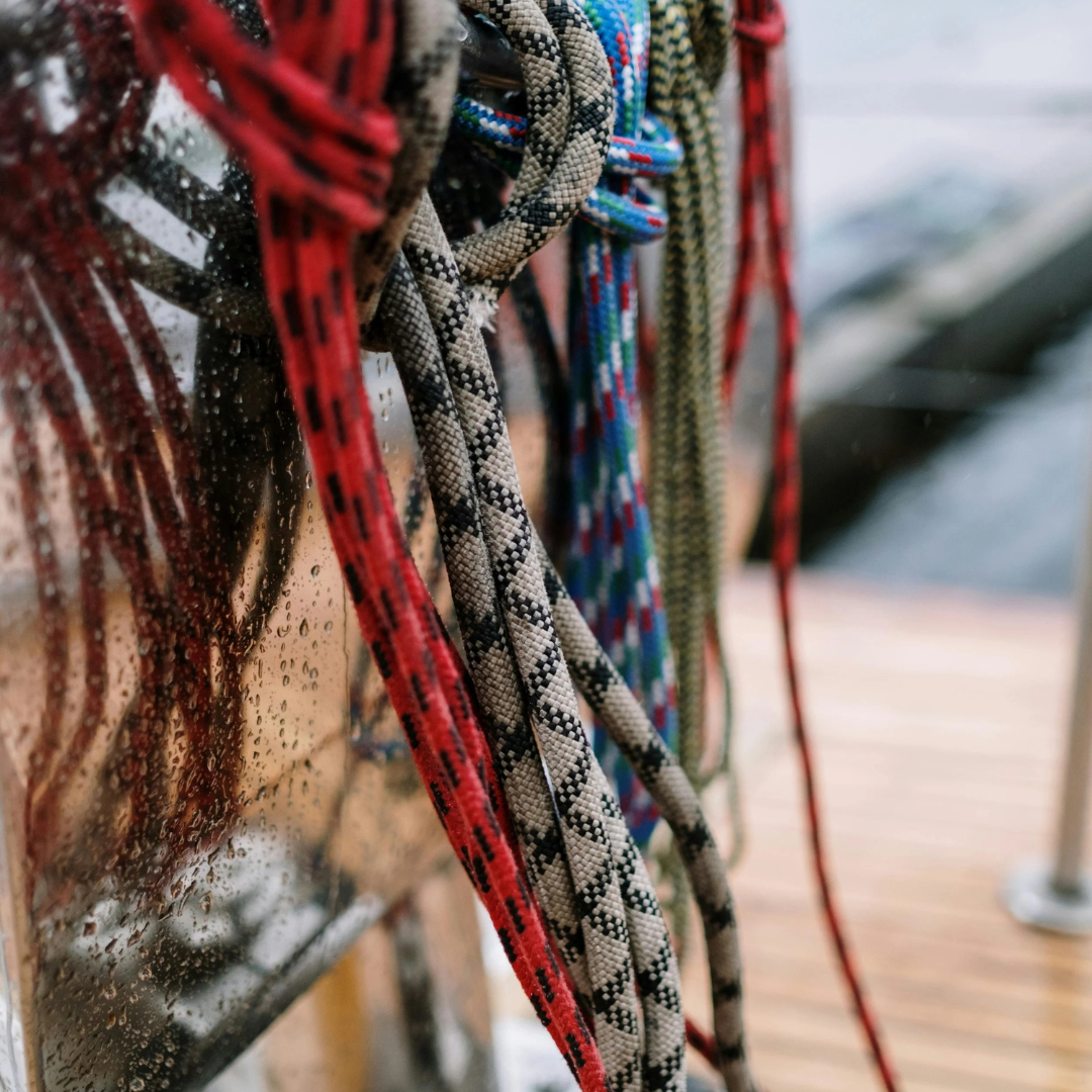 Close-up of multiple climbing ropes hanging against a wet, rain-covered surface, with a blurred background.