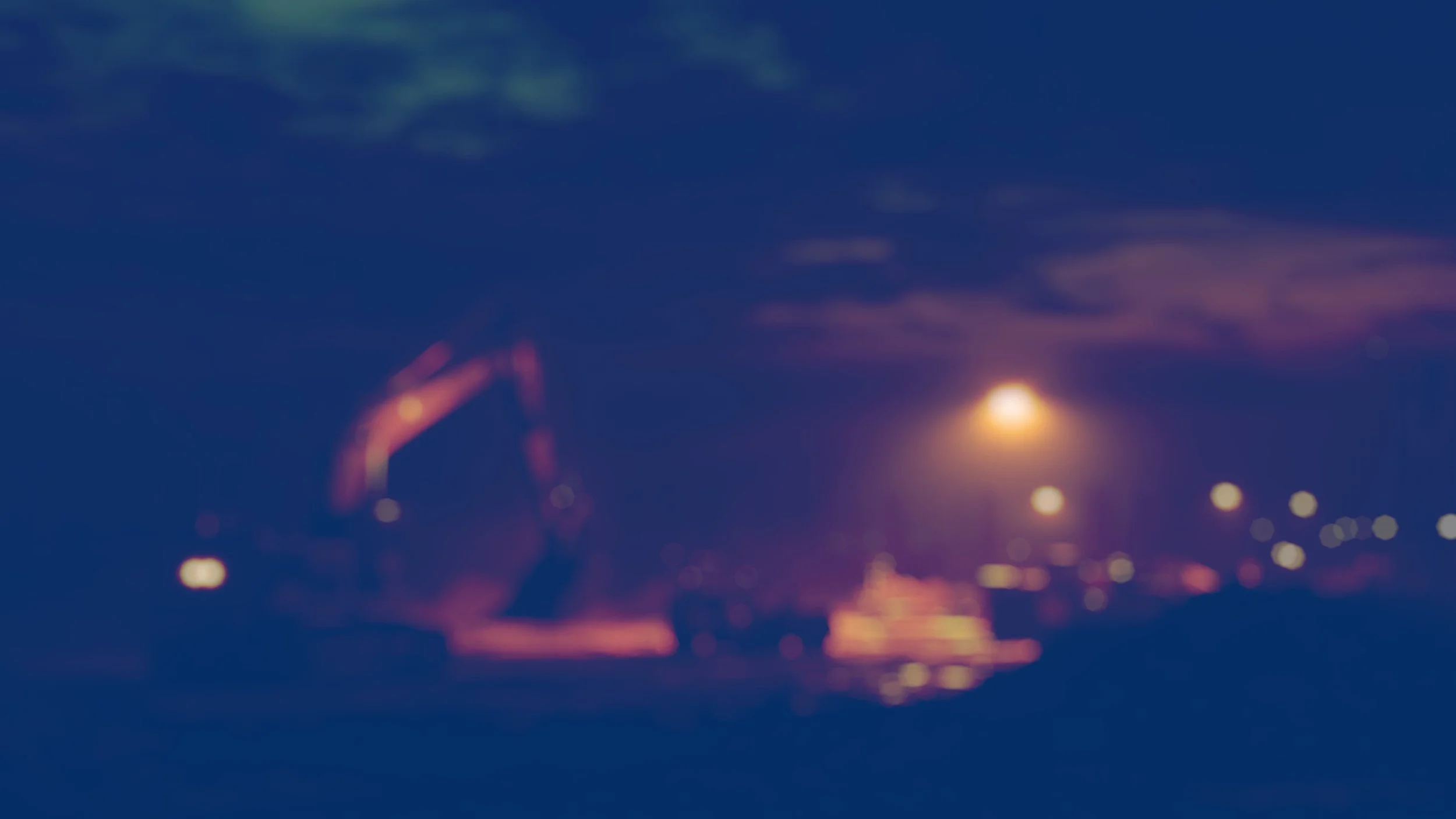 A blurred image of a machine with an arch structure on the ground at night, illuminated by lights, with a bright light or moon in the sky and clouds overhead.