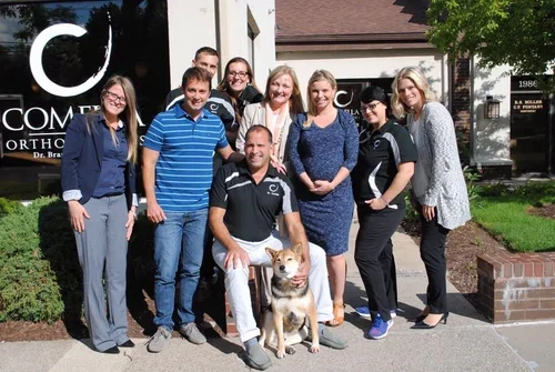 Grupo de personas y un perro posando afuera de una clínica u oficina de odontología.
