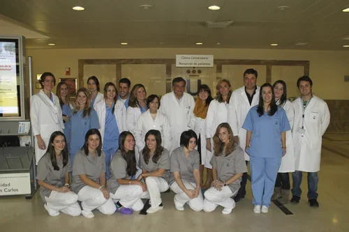 Grupo de profesionales de la salud, algunos en batas blancas y otros en uniforme azul y gris, posando en un hospital o clínica.