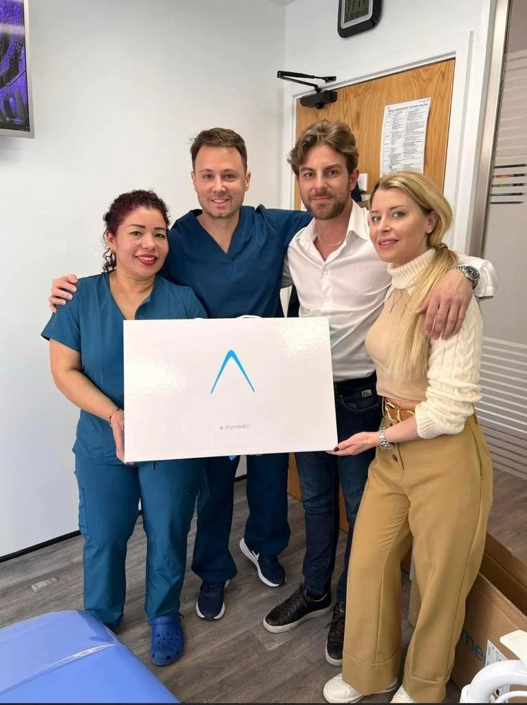 Cuatro personas en un hospital sosteniendo una caja grande con logo azul y la palabra 'skymedic', en una sala de atención médica.