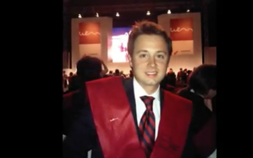 Joven con toga de graduación en una ceremonia en un auditorio.