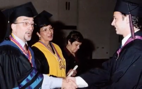 Graduados en toga y birrete estrechándose la mano en una ceremonia de graduación.