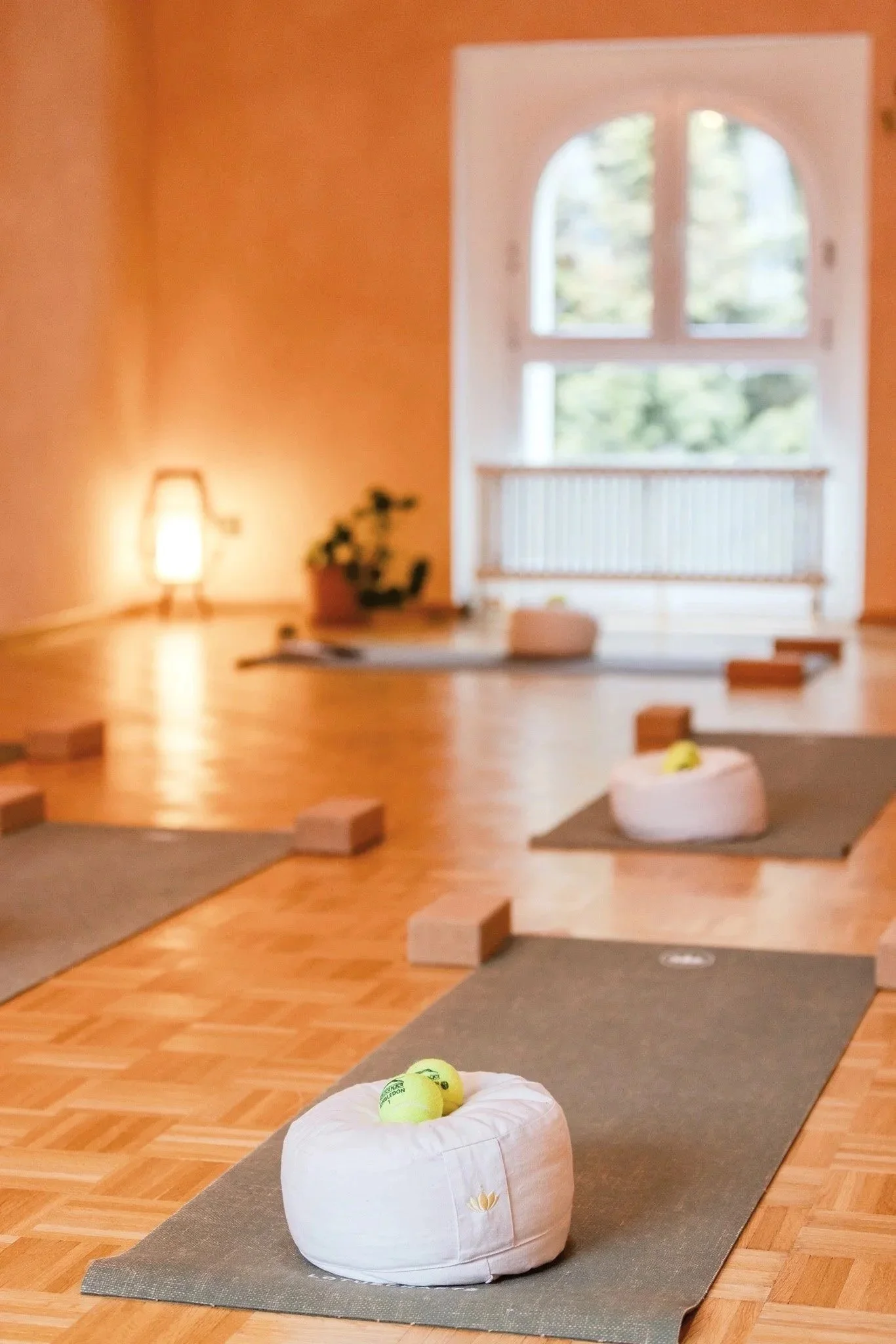 Yoga-Raum mit Yoga-Matten, Yogablock, Tennisbällen und weichen Sitzkissen, große Fenster, Holzboden, warmes Licht. Yoga Bern Fischermätteli.