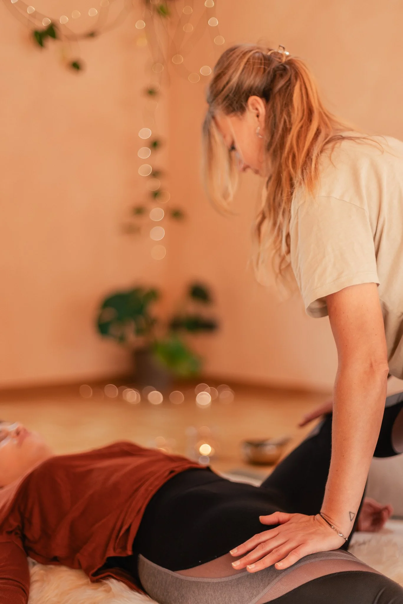 Zwei Frauen führen in einem gemütlich dekorierten Raum eine Yoga-Übung durch. Eine Frau liegt auf dem Rücken, die andere Frau unterstützt sie, während sie eine Yoga-Position eingenommen hat. Thai Yoga Massage Bern.