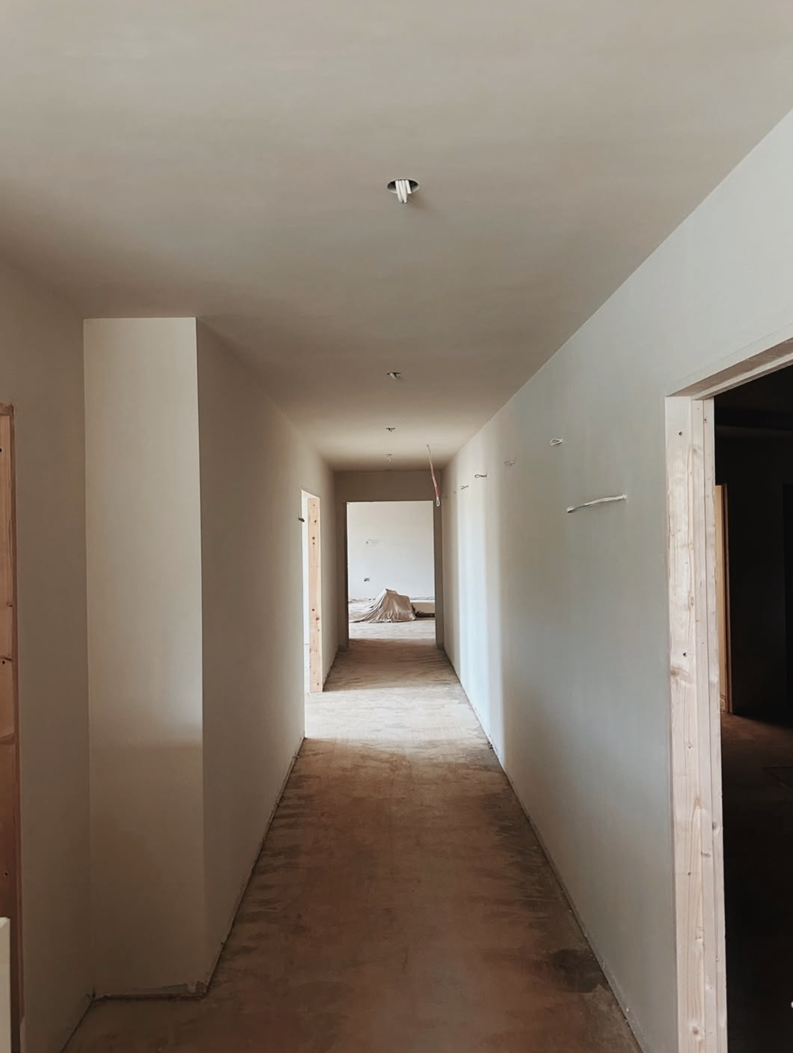 Interior view of a reformer pilates studio under construction, showing a hallway with white walls, flooring, and exposed door frames.