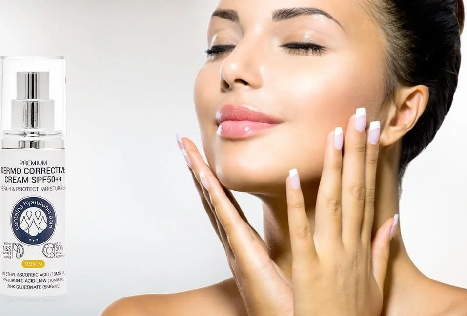 A woman with clear skin touching her face with both hands, smiling softly with eyes closed. There is a bottle of skin care cream with SPF on the left side of the image.