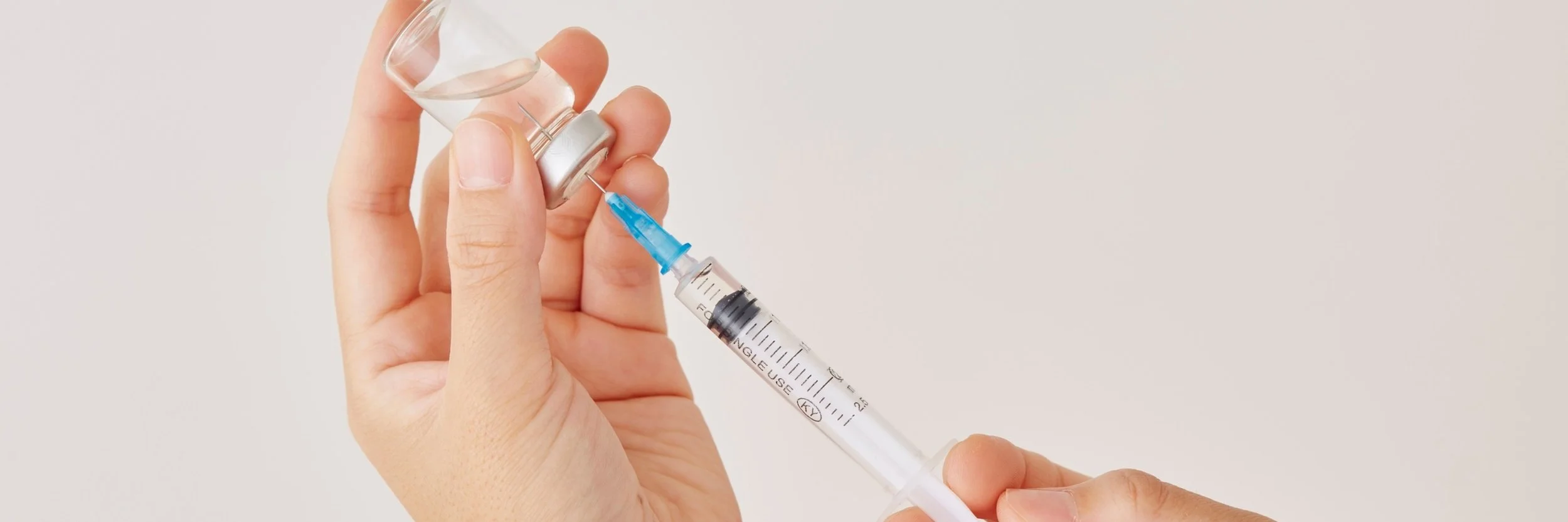 A hand holding a small glass vial to promote vitamin injections