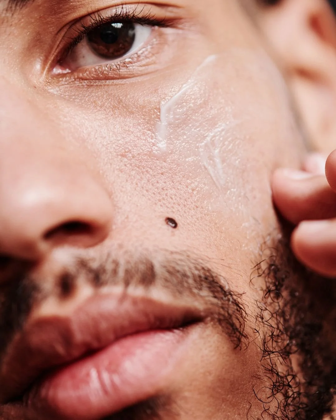 Close-up of a man's face showing him applying a skincare product to his cheek.