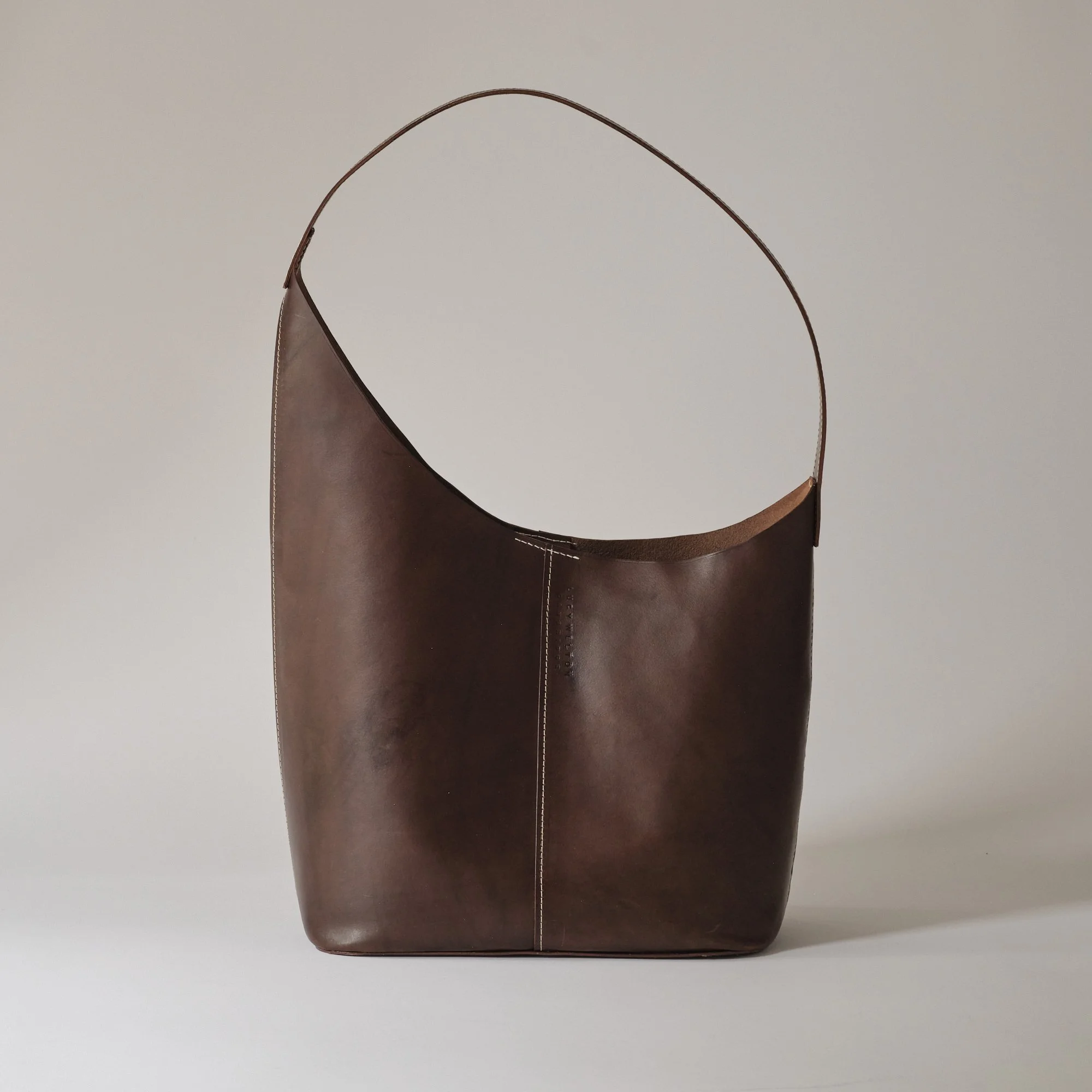 A brown leather shoulder bag with a simple design against a plain background.