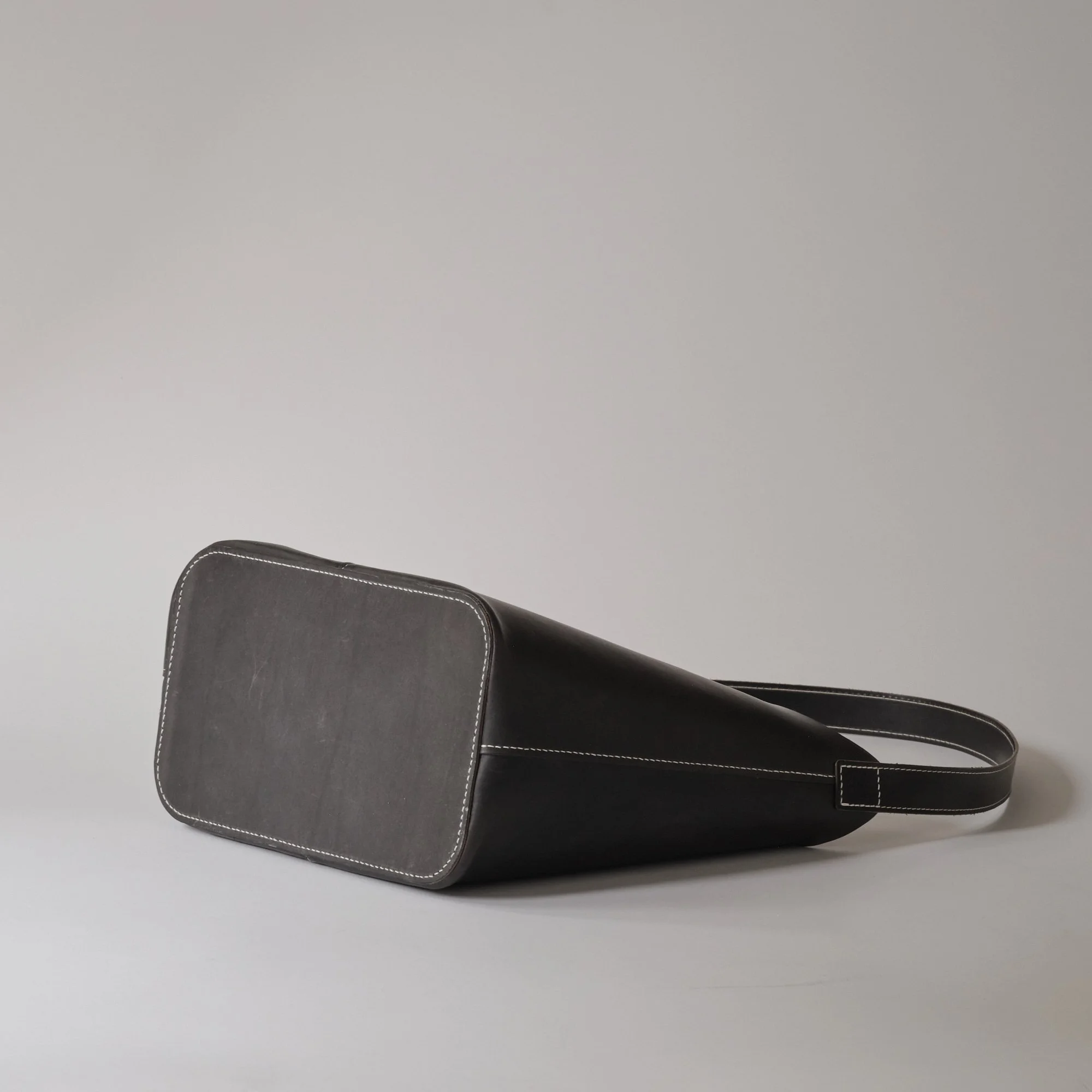 A black leather handbag with white stitching and a long strap, resting on a plain white surface.