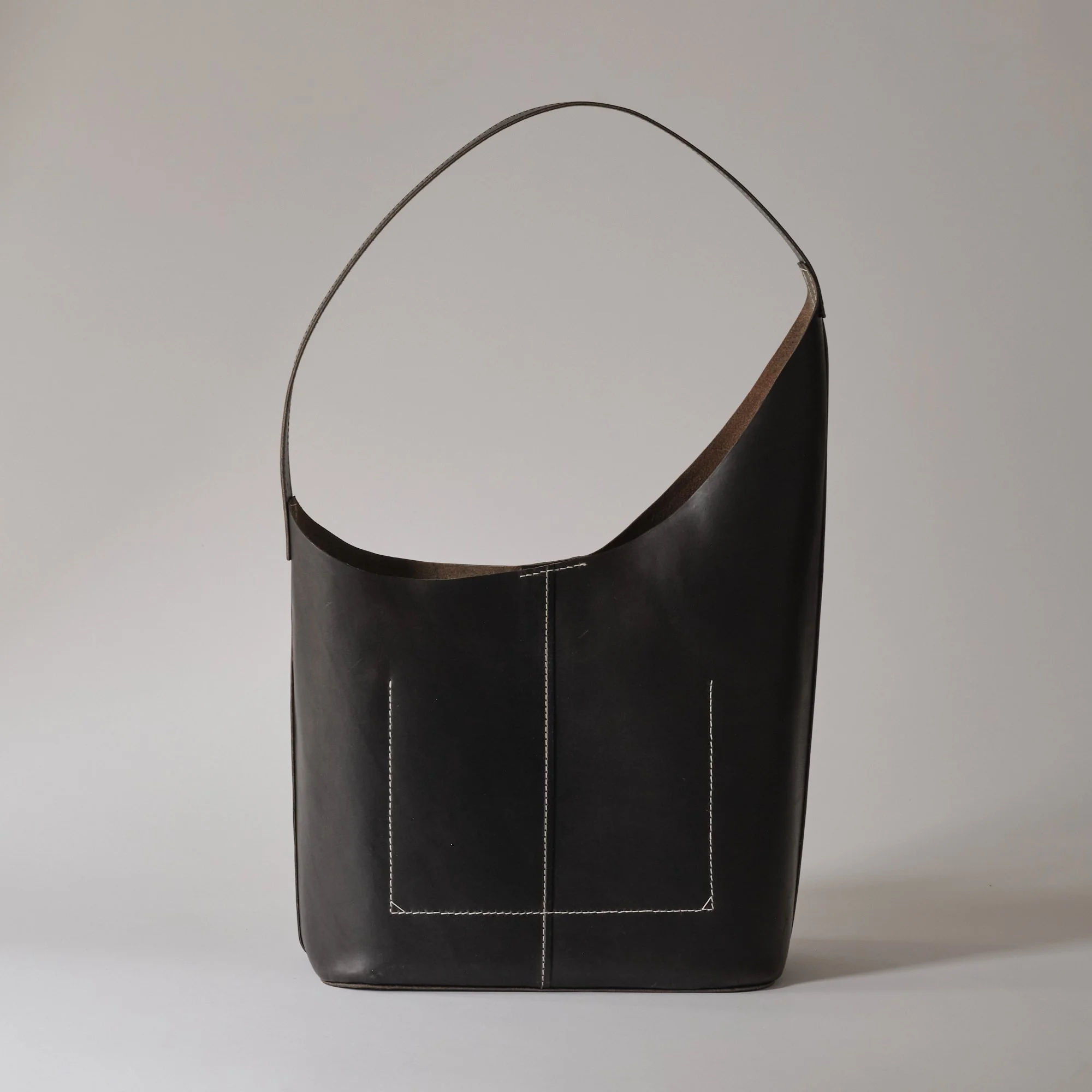 Black leather tote bag with white stitching, set against a plain gray background.