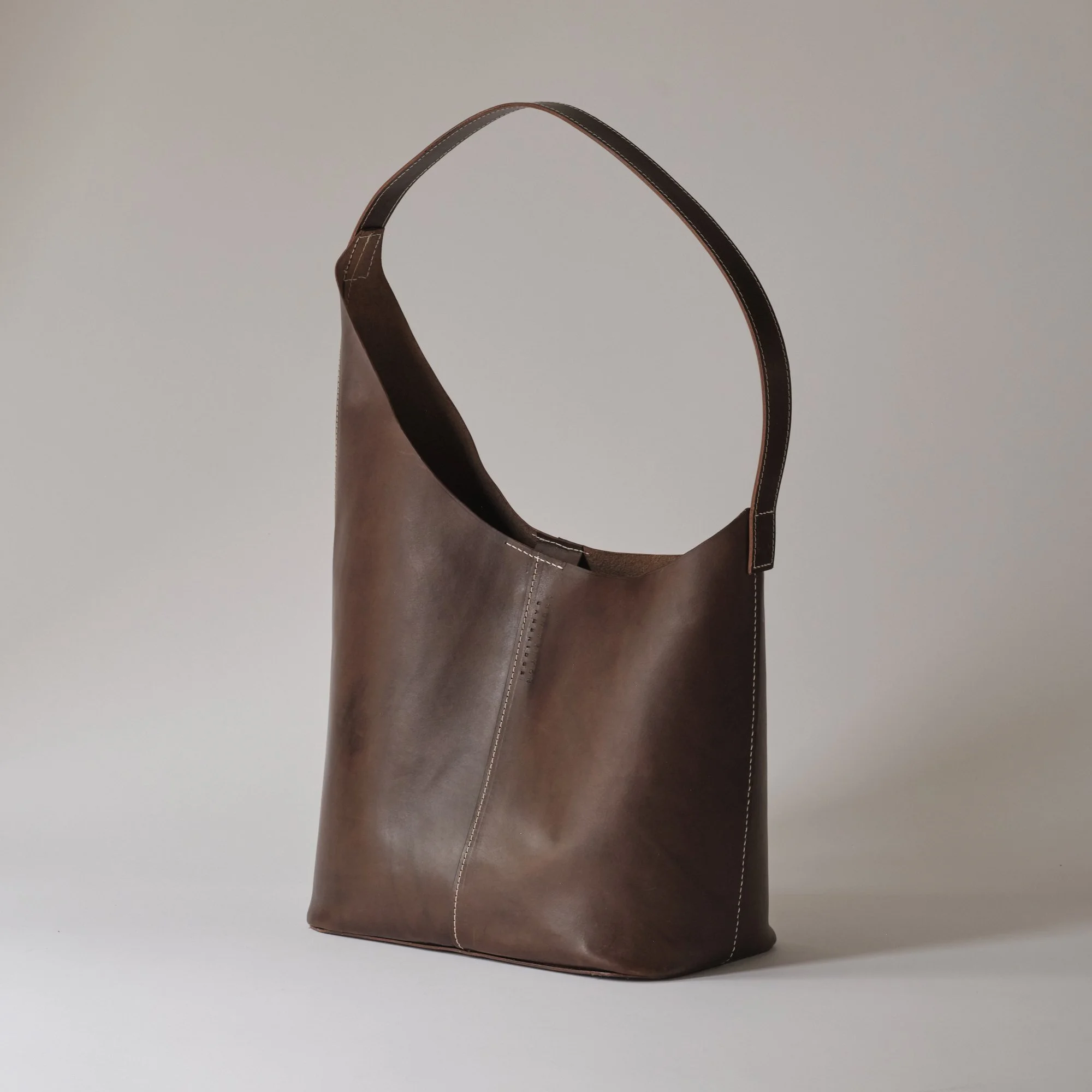 Brown leather tote bag with a shoulder strap on a plain background.