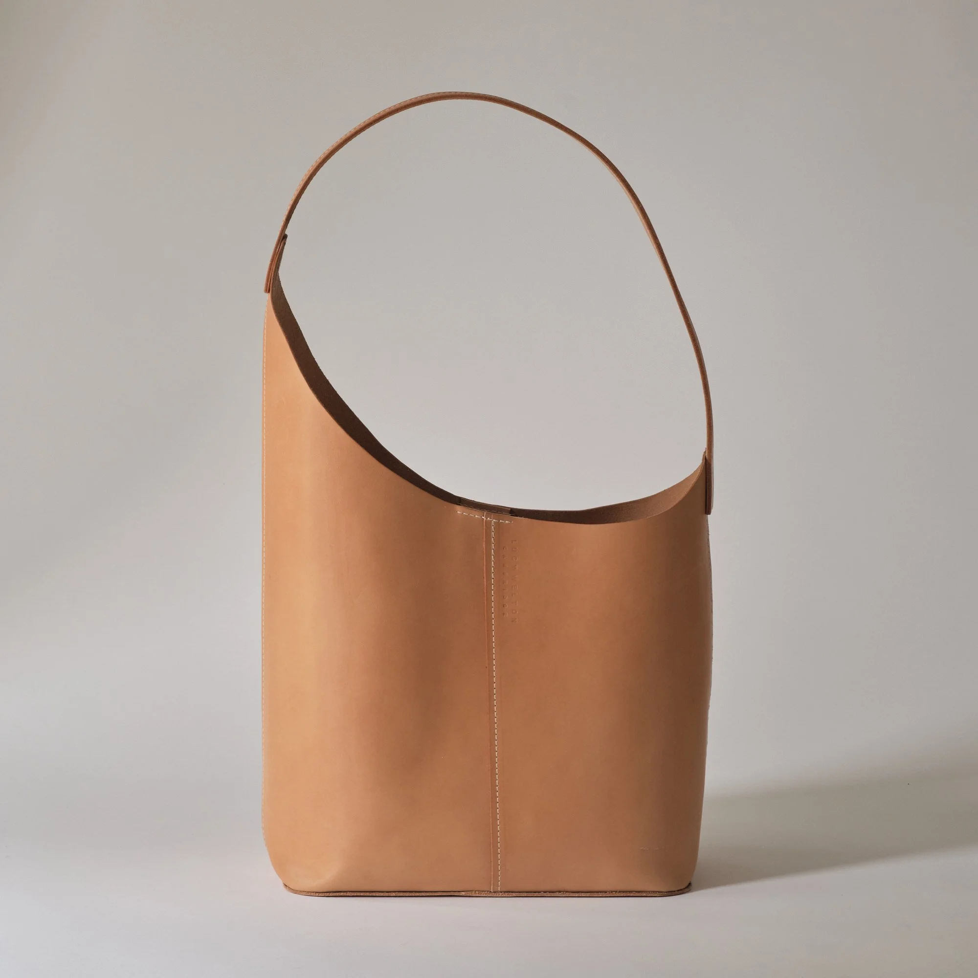 A tan leather handbag with a curved single strap, standing upright against a plain light background.