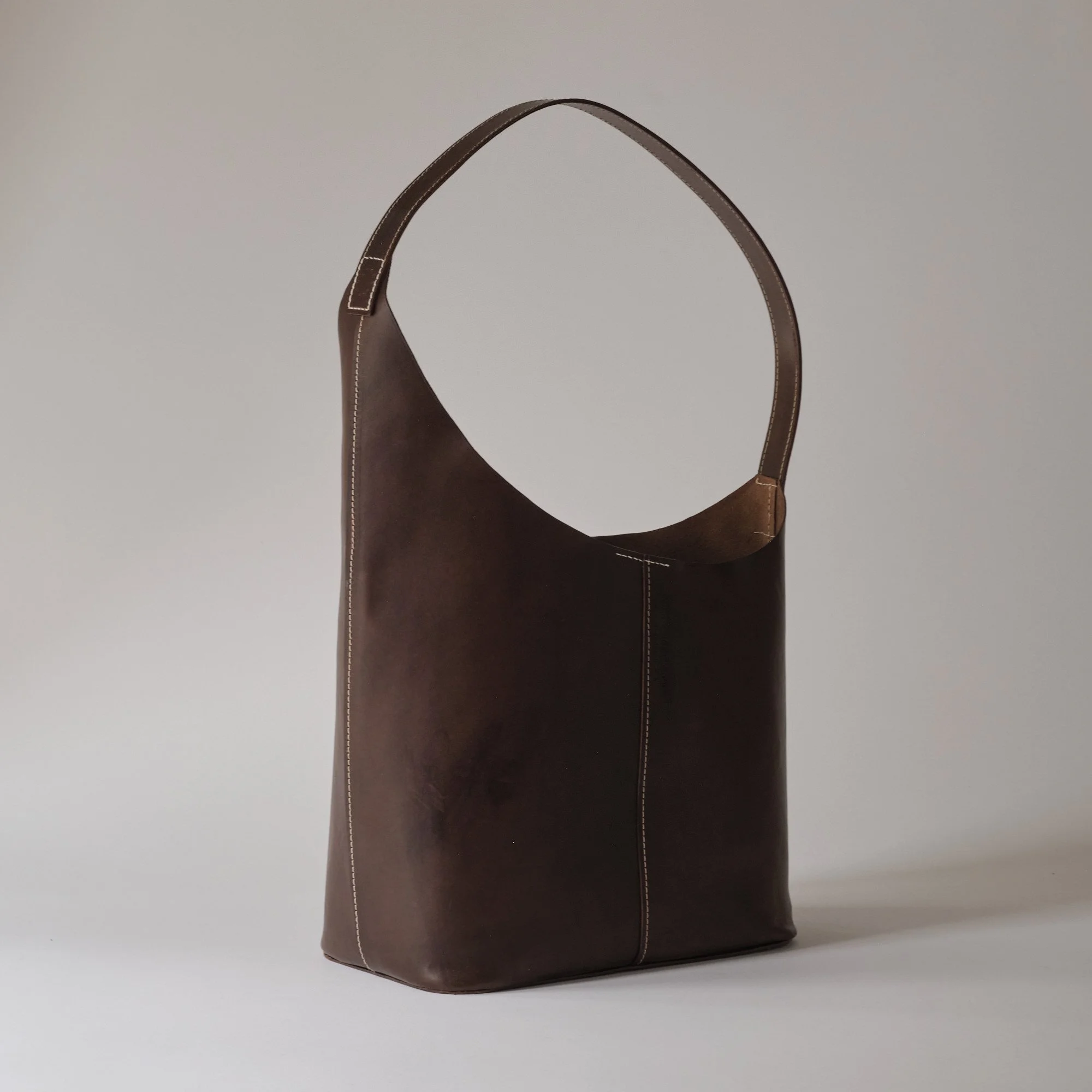 Brown leather tote bag with white stitching, positioned upright on a plain background.