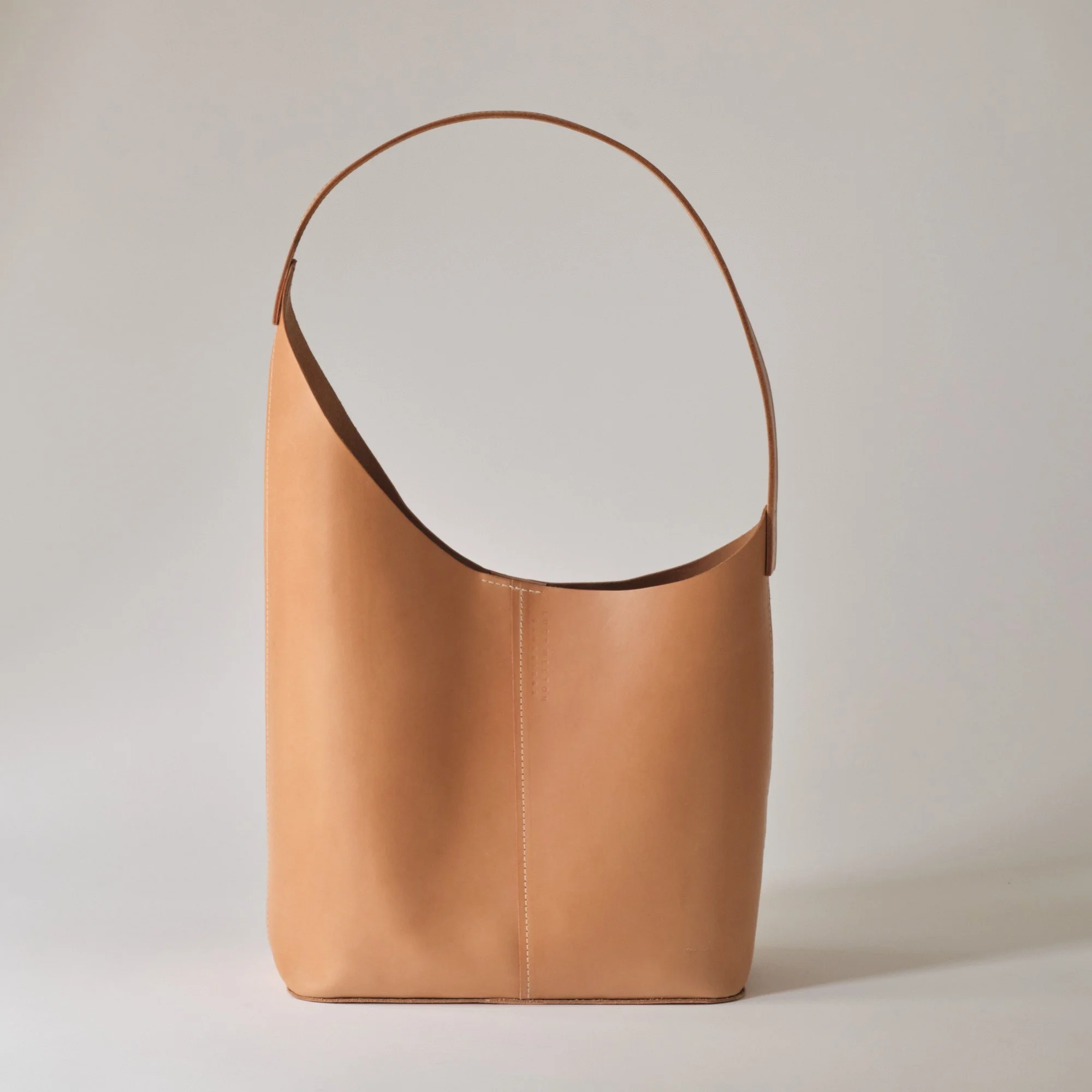 A tan leather handbag with a single strap, standing upright against a plain background.