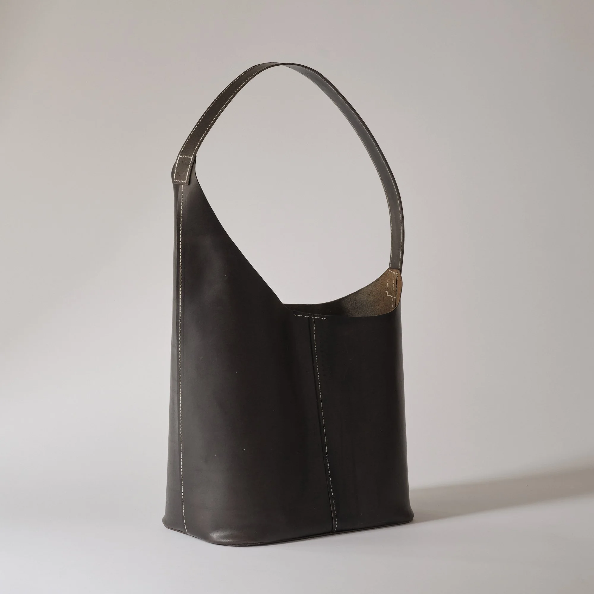 Black leather tote bag with white stitching on a light gray background.