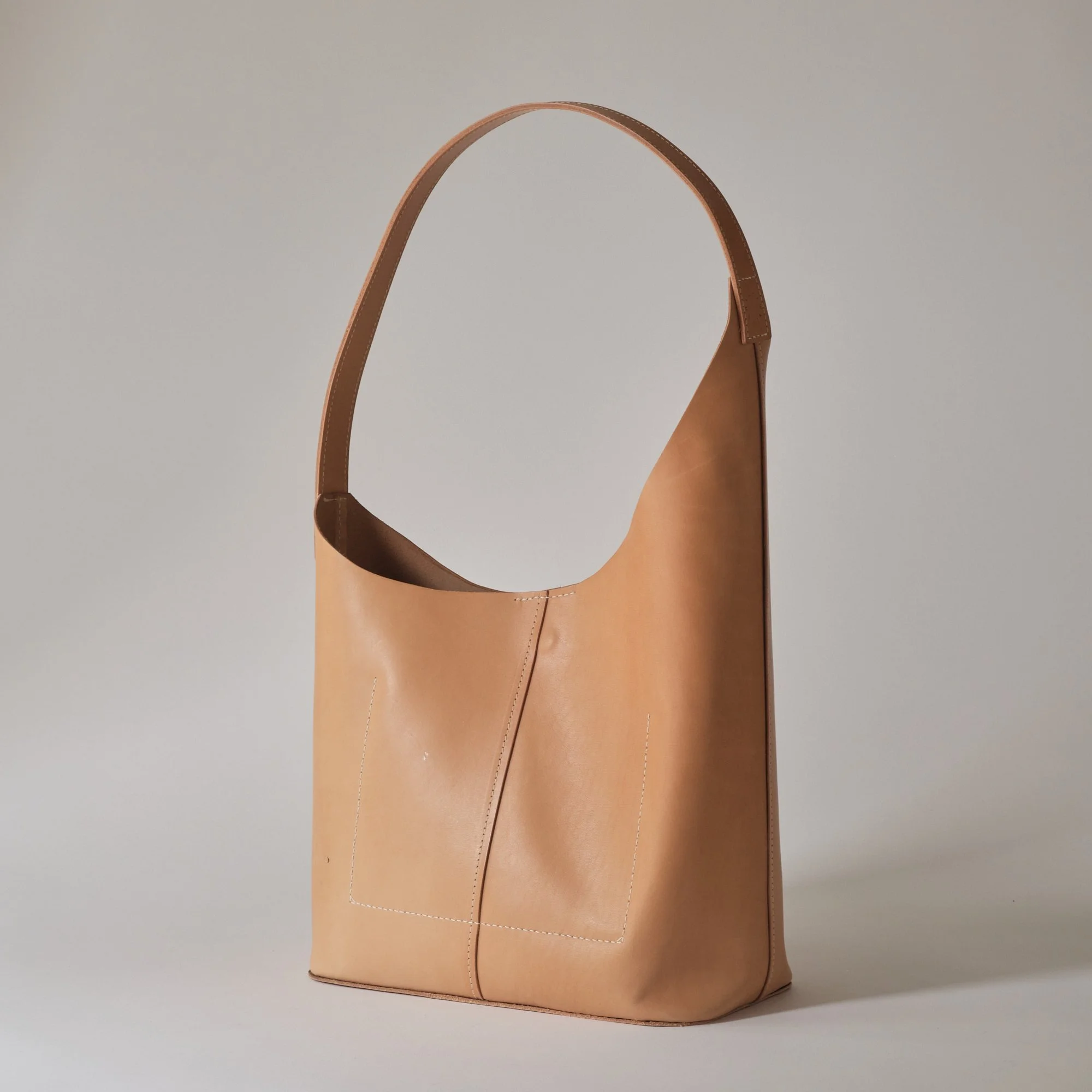 A tan leather tote bag with a single shoulder strap against a light background.