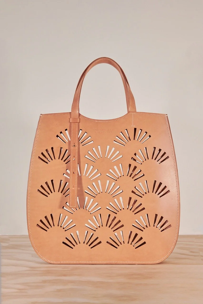 A tan tote bag with an intricate pattern of cut-out fan shapes on its surface.