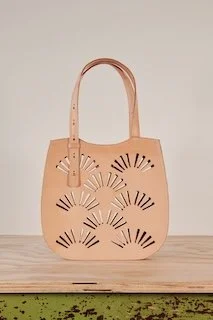 Beige tote bag with cutout fan designs on the front, placed on a wooden surface.