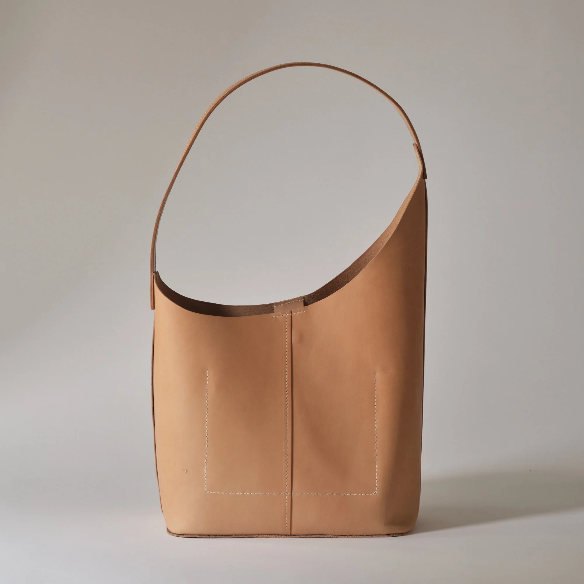 A tan leather tote bag with a simple, rectangular shape and a single shoulder strap, sitting on a neutral background.