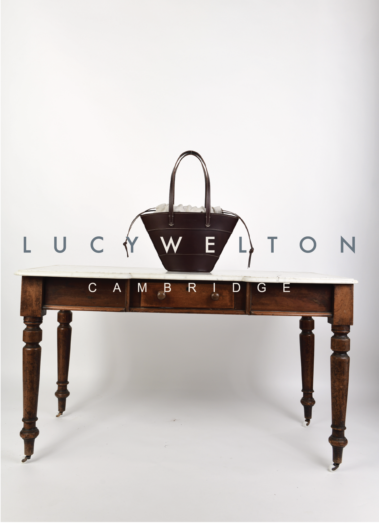 A black handbag with white interior on a wooden table with white background, featuring the text "LUCY WELTON CAMBRIDGE" across the image.
