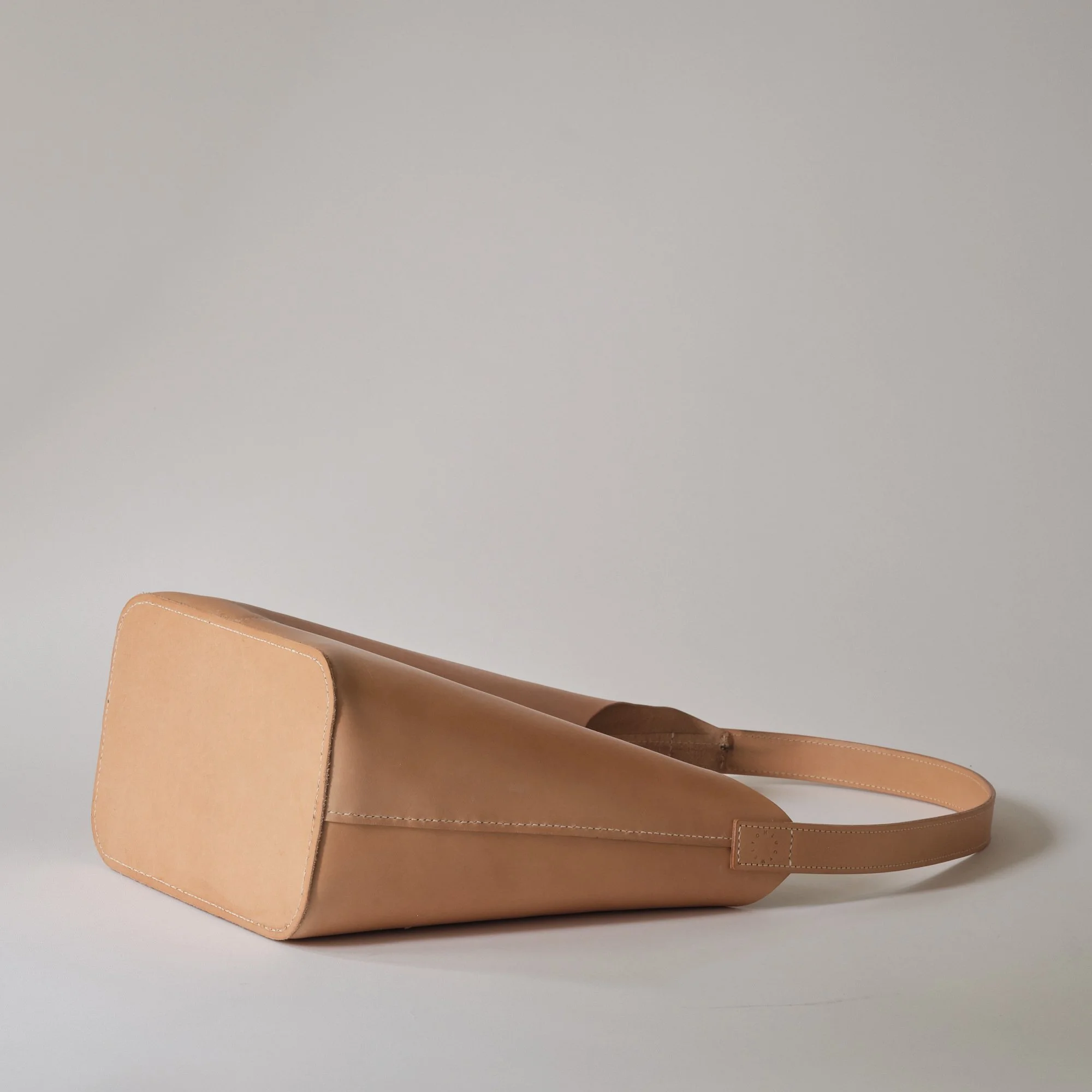 A beige leather handbag placed on a light gray surface.