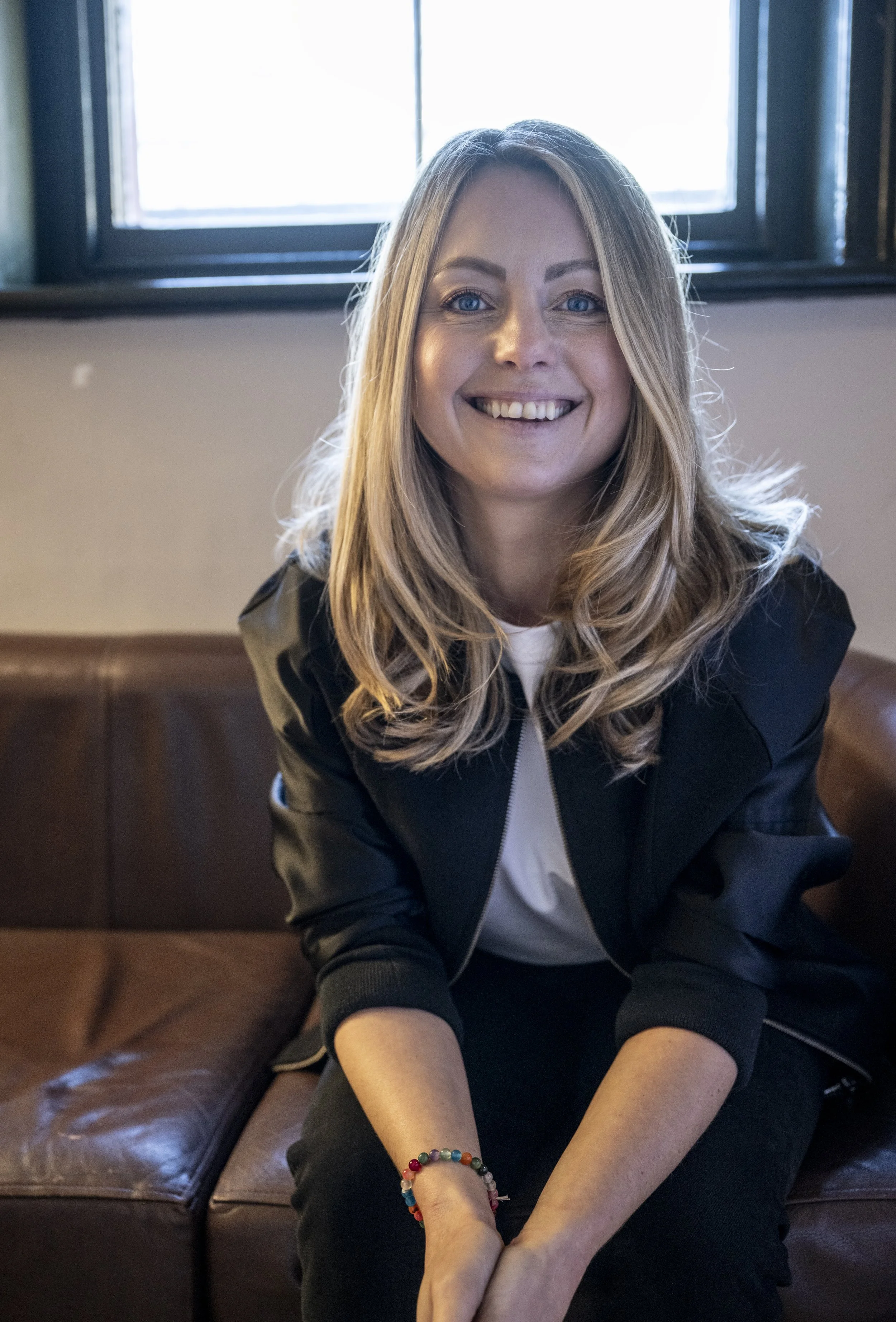 Coach, consultant & strategist for the music, tech and creative industries, Nicola Fuller, smiling on a leather couch in a brightly lit studio.
