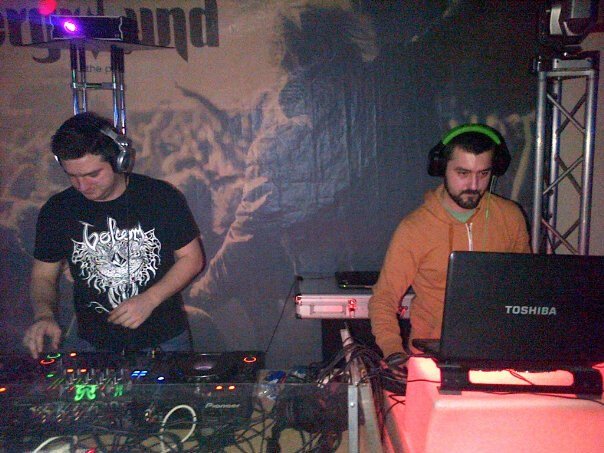Two men DJing at a music event with DJ equipment and headphones.