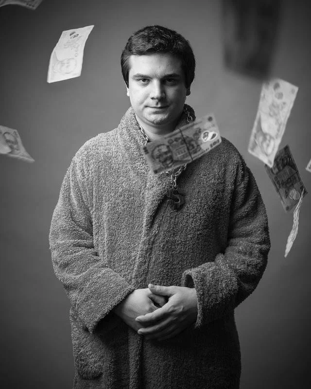 A young man standing in front of a plain background, wearing a textured fuzzy jacket, with floating banknotes around him.