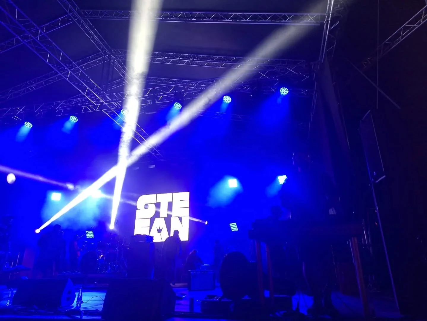 Stage with blue lighting, stage equipment, and a large LED screen displaying the name 'STEAEN'.