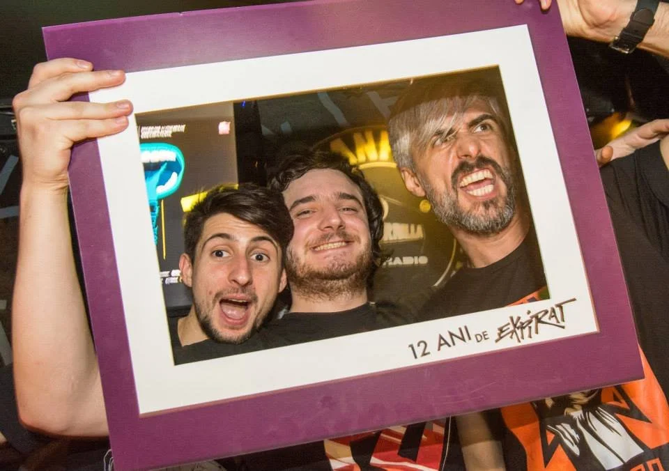 Three men behind a large purple photo frame, smiling and making silly faces at the camera at a celebration for 12 years of Epektat.