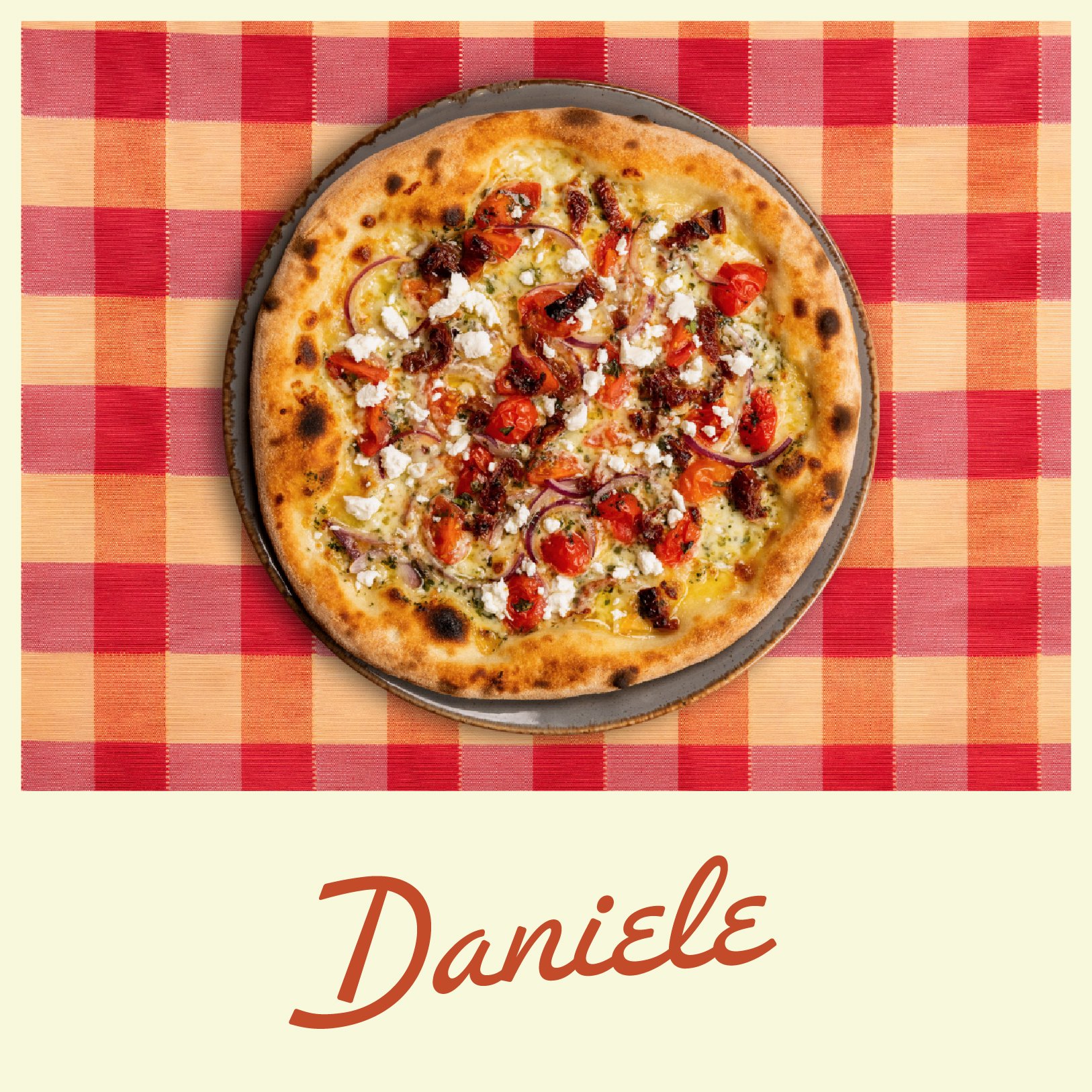 A pizza topped with cherry tomatoes, red onions, crumbled cheese, and sausage slices on a plate, with a red checkered tablecloth background.