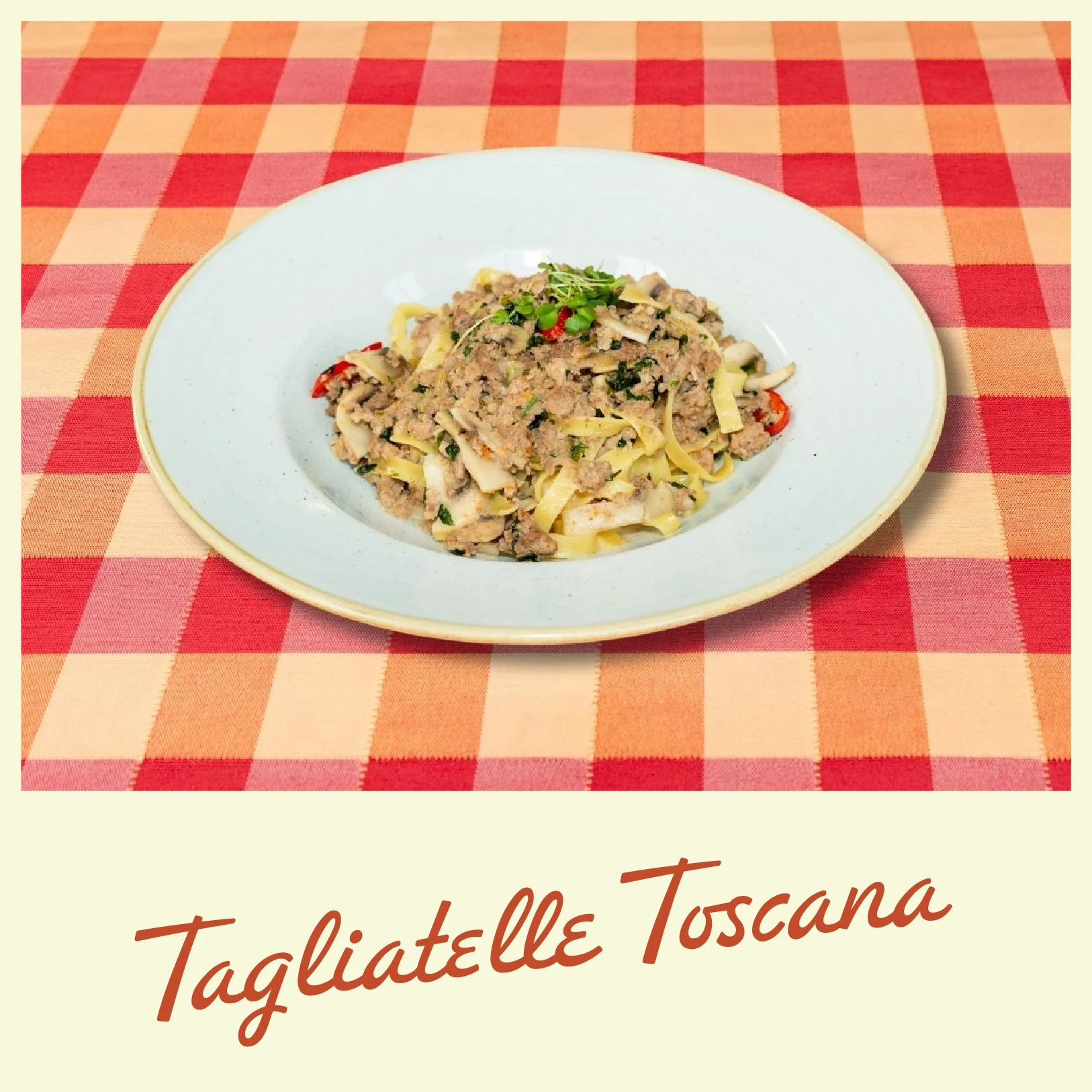 A bowl of pumpkin soup topped with croutons, pumpkin seeds, and herbs on a red and orange checkered tablecloth.