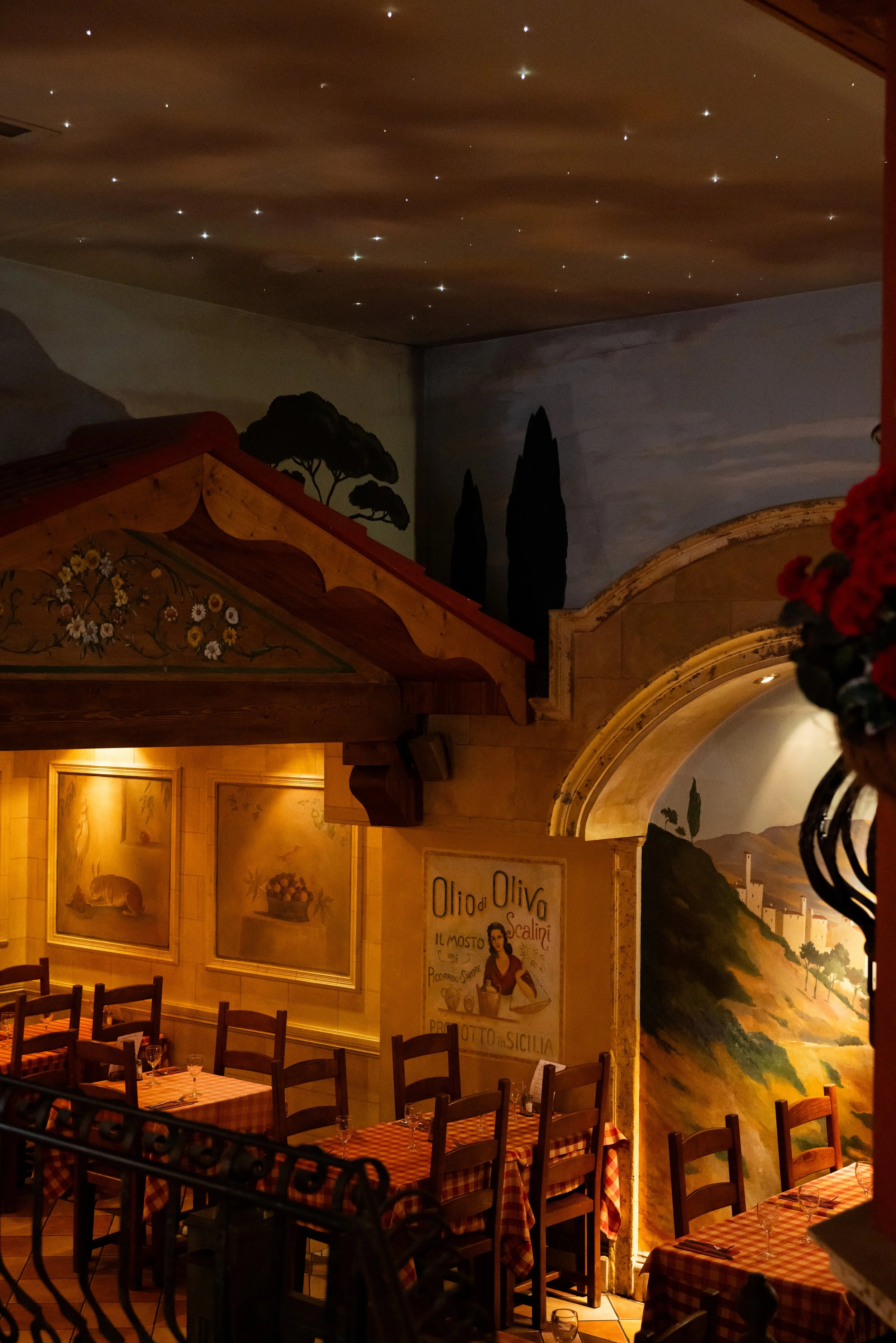 Interior of a restaurant with wooden tables and chairs, painted murals depicting landscapes, and a ceiling with star-like lights.