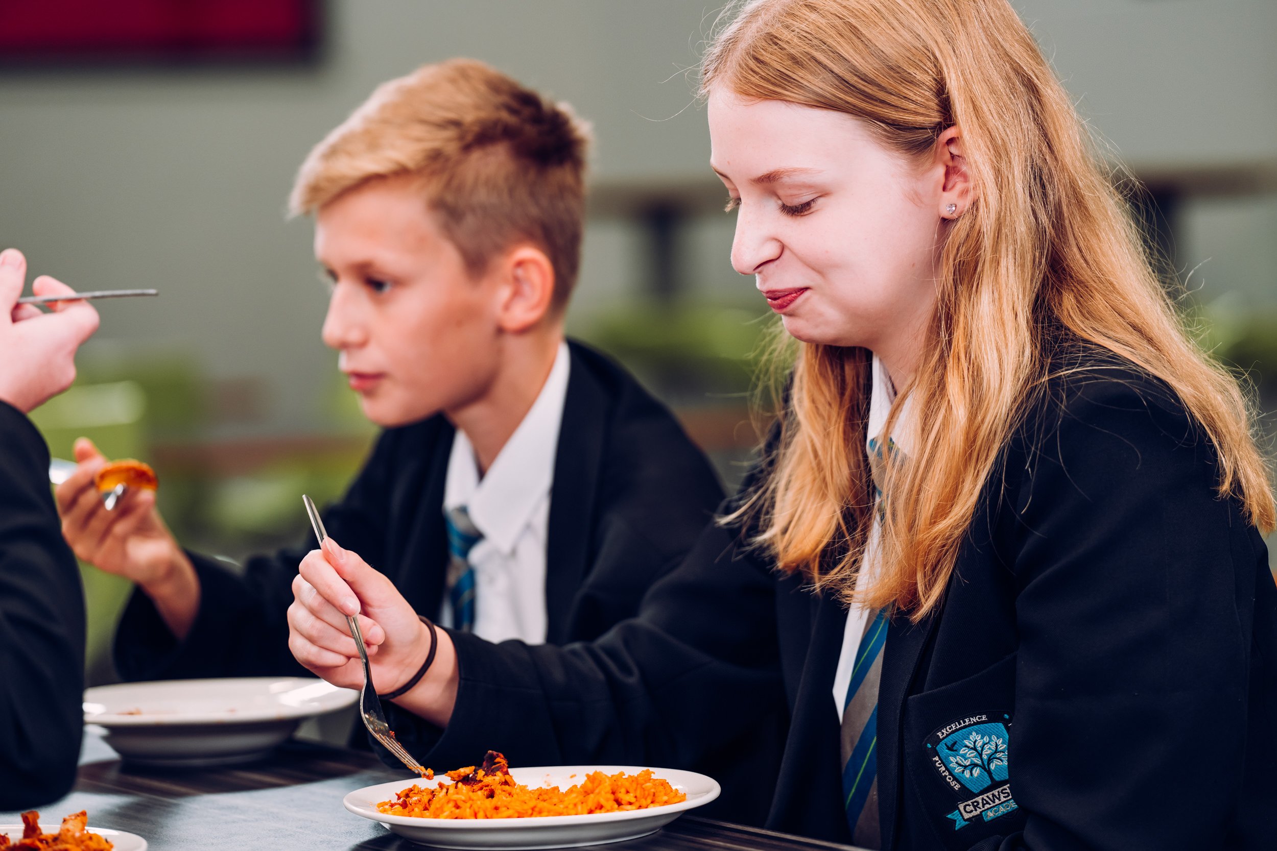 Two teenagers in school uniforms eating spaghetti at a table.