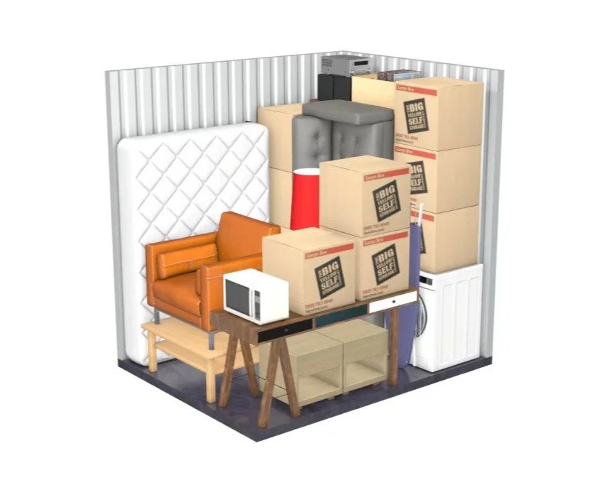 A storage unit filled with furniture and household items, including a mattress, sofa, microwave, stacked boxes, lamp, washing machine, and cleaning supplies.