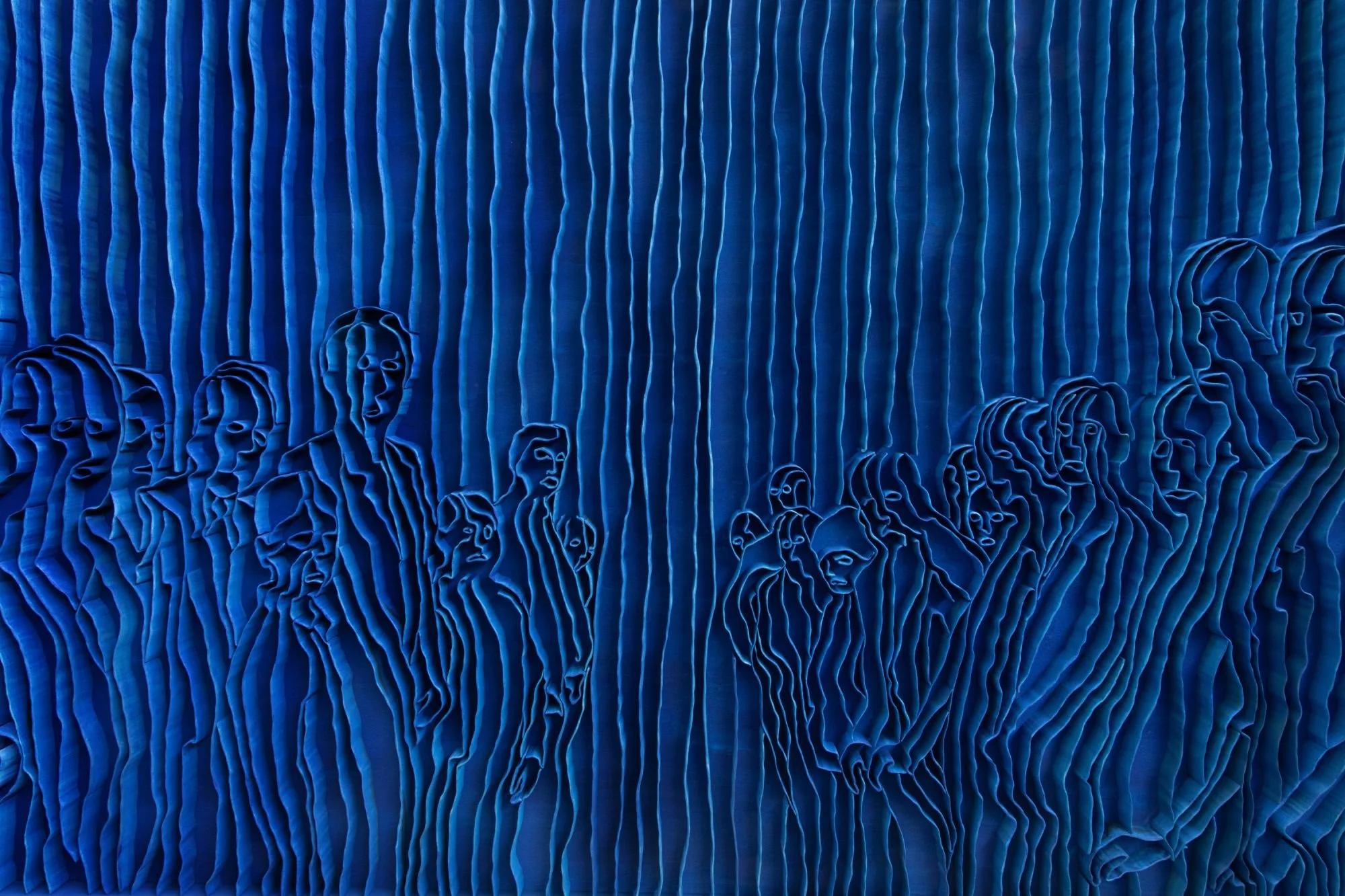 Blue textured art installation with abstract human faces and vertical ridges.
