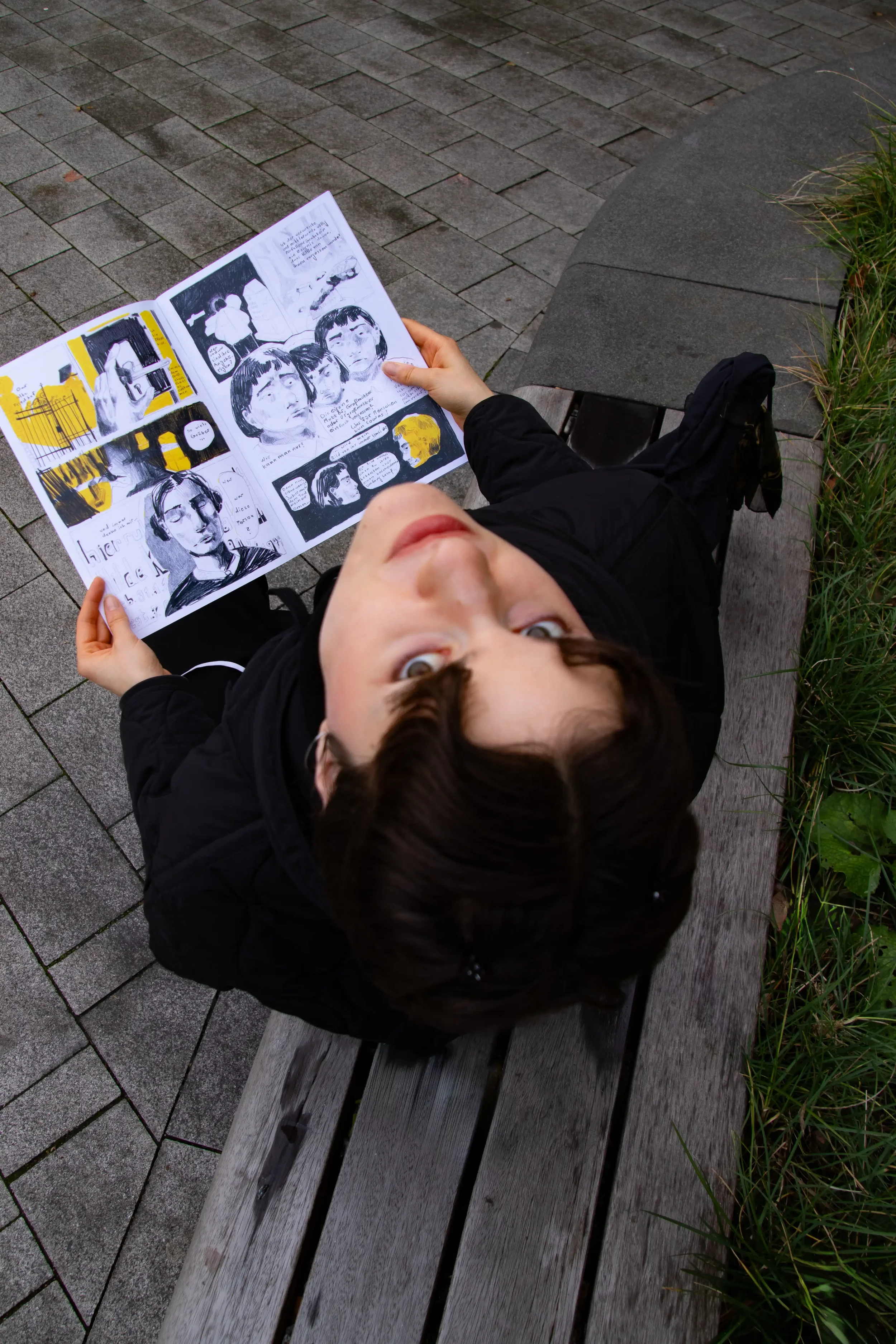 Junge Frau sitzt auf einer Bank im Freien und liest einen Comic-Strip, Blick nach oben gerichtet.