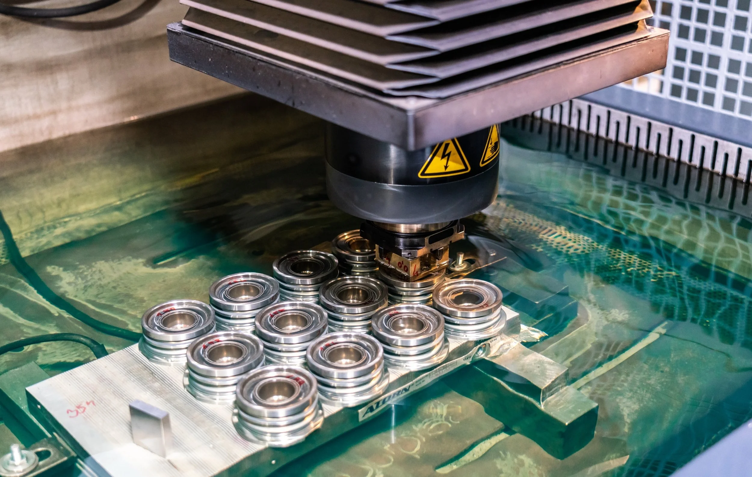 A robotic arm placing metal bearings into a mold submerged in liquid on a manufacturing process.