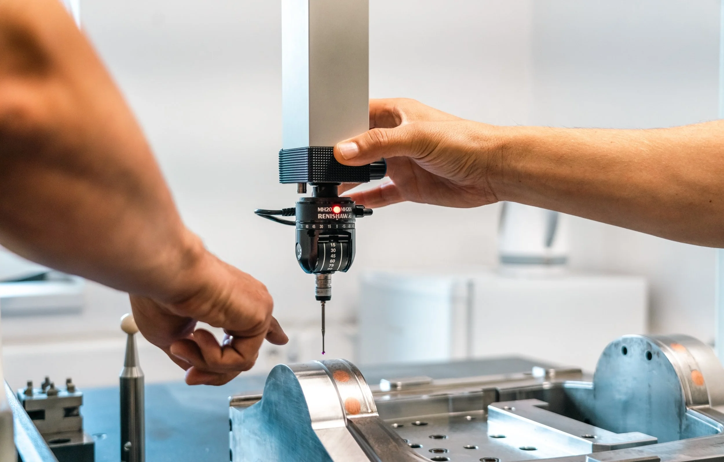 Close-up of a person’s hands using a precision tool on a metallic device or part, possibly in a laboratory or manufacturing setting.