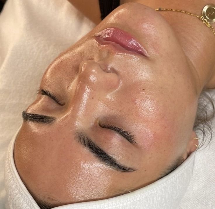 Close-up of a woman lying with her eyes closed after a skincare treatment, showing her smooth, glowing skin and eyebrows.