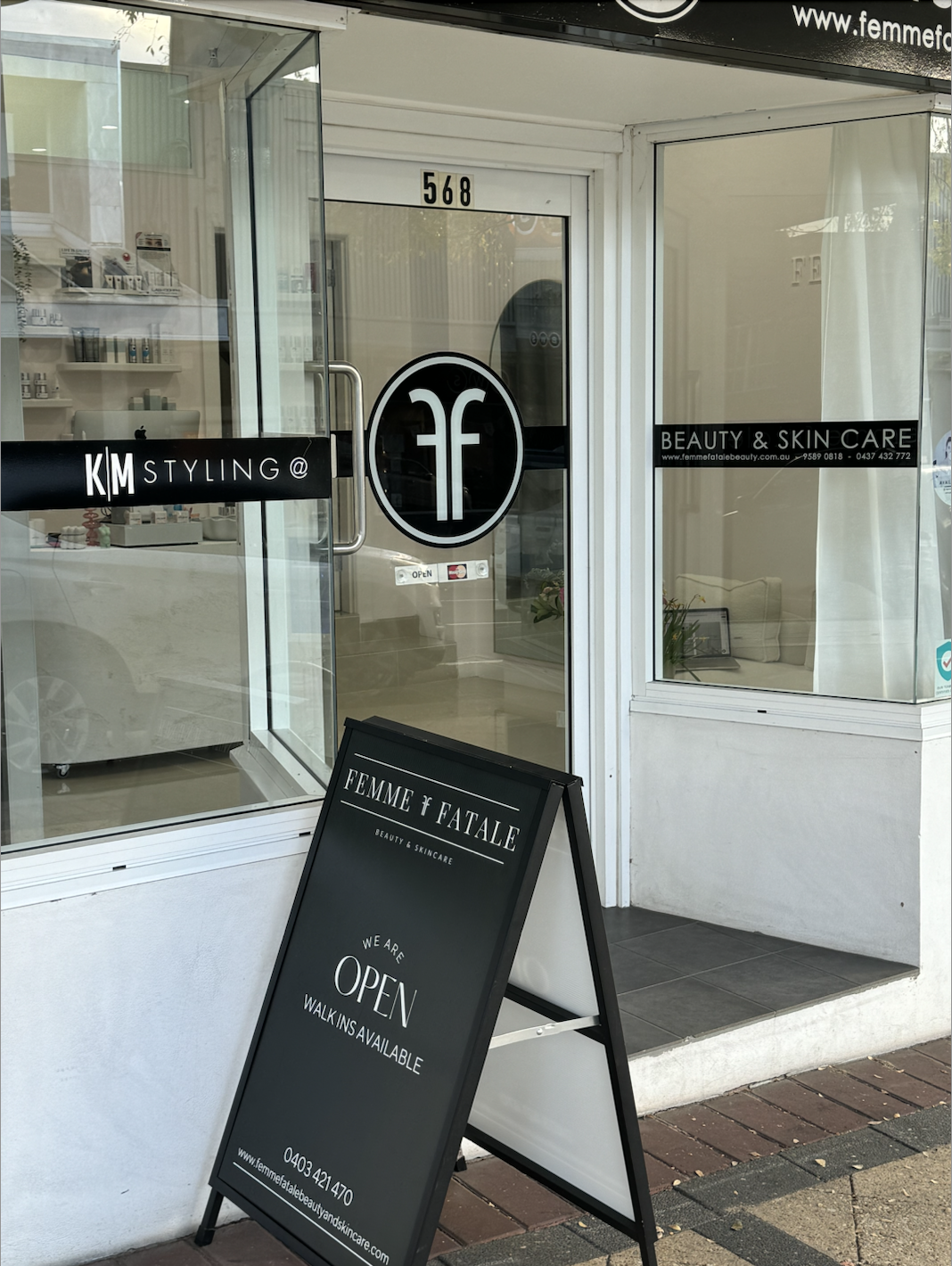 Exterior of Femme Fatale Beauty & Skincare salon with a black sidewalk sign indicating it is open and walk-ins are available, located at 568. The salon's logo and signs are visible on the windows and door.