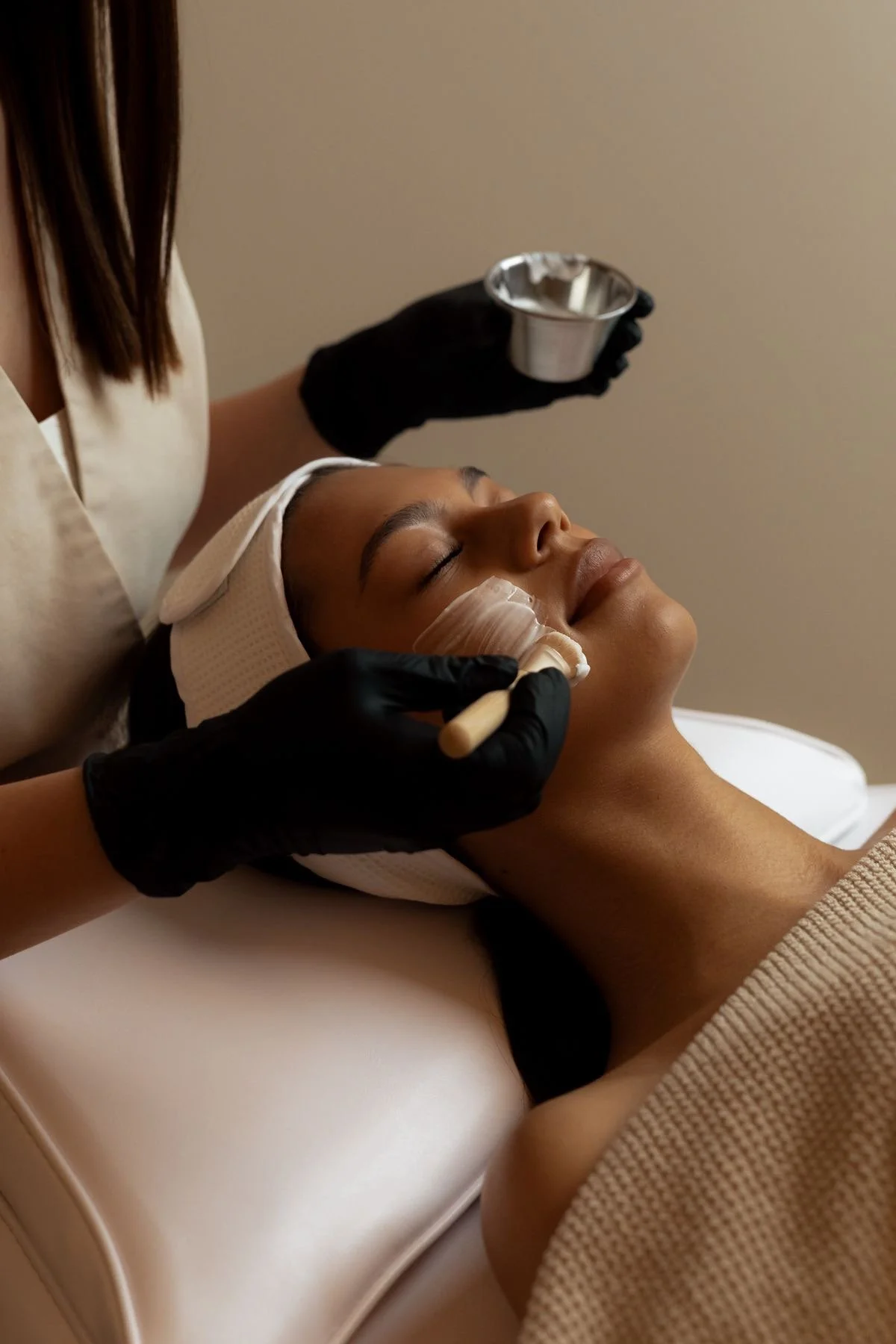 A woman getting a facial treatment at a spa, with facial mask application, while lying down with eyes closed.